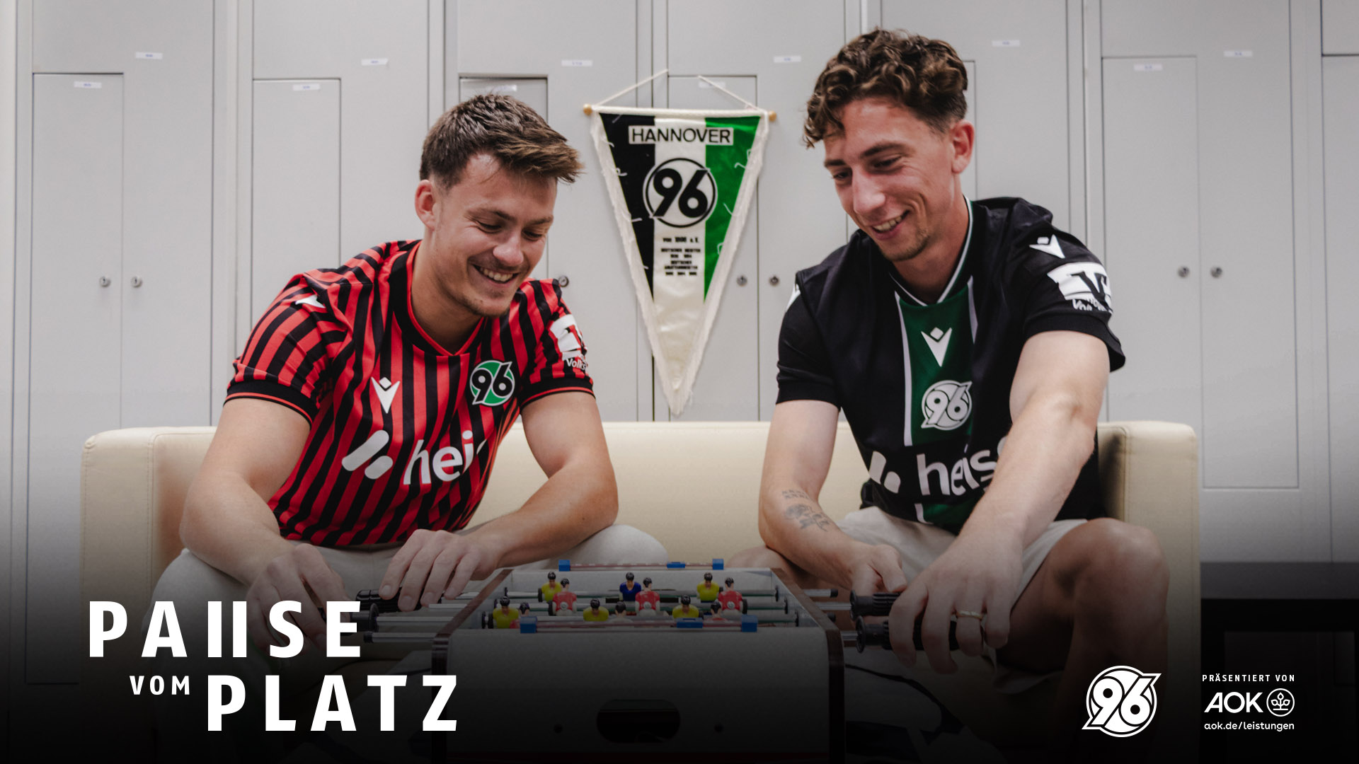 Host Niklas (links) und Rochelt sitzen auf dem Sofa und spielen Tischfußball.
