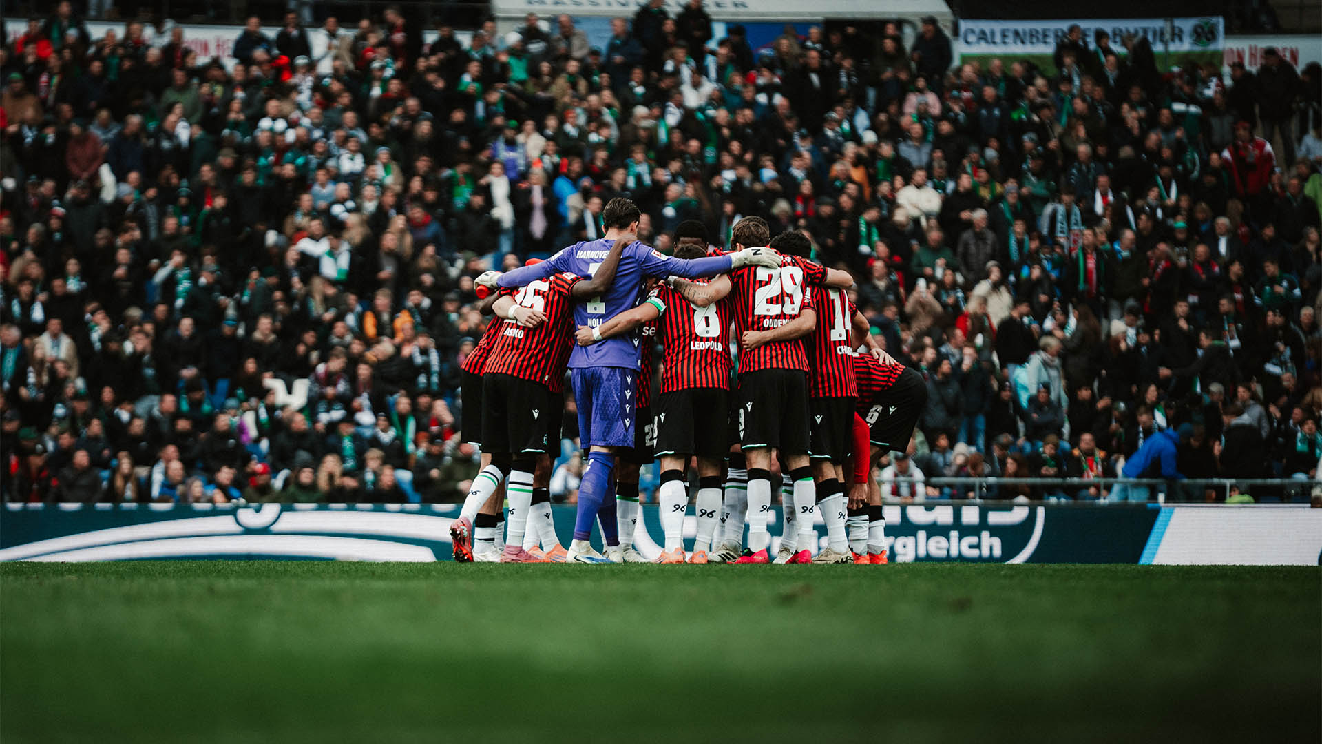 Mannschaftskreis im Stadion, dahinter volle Ränge.