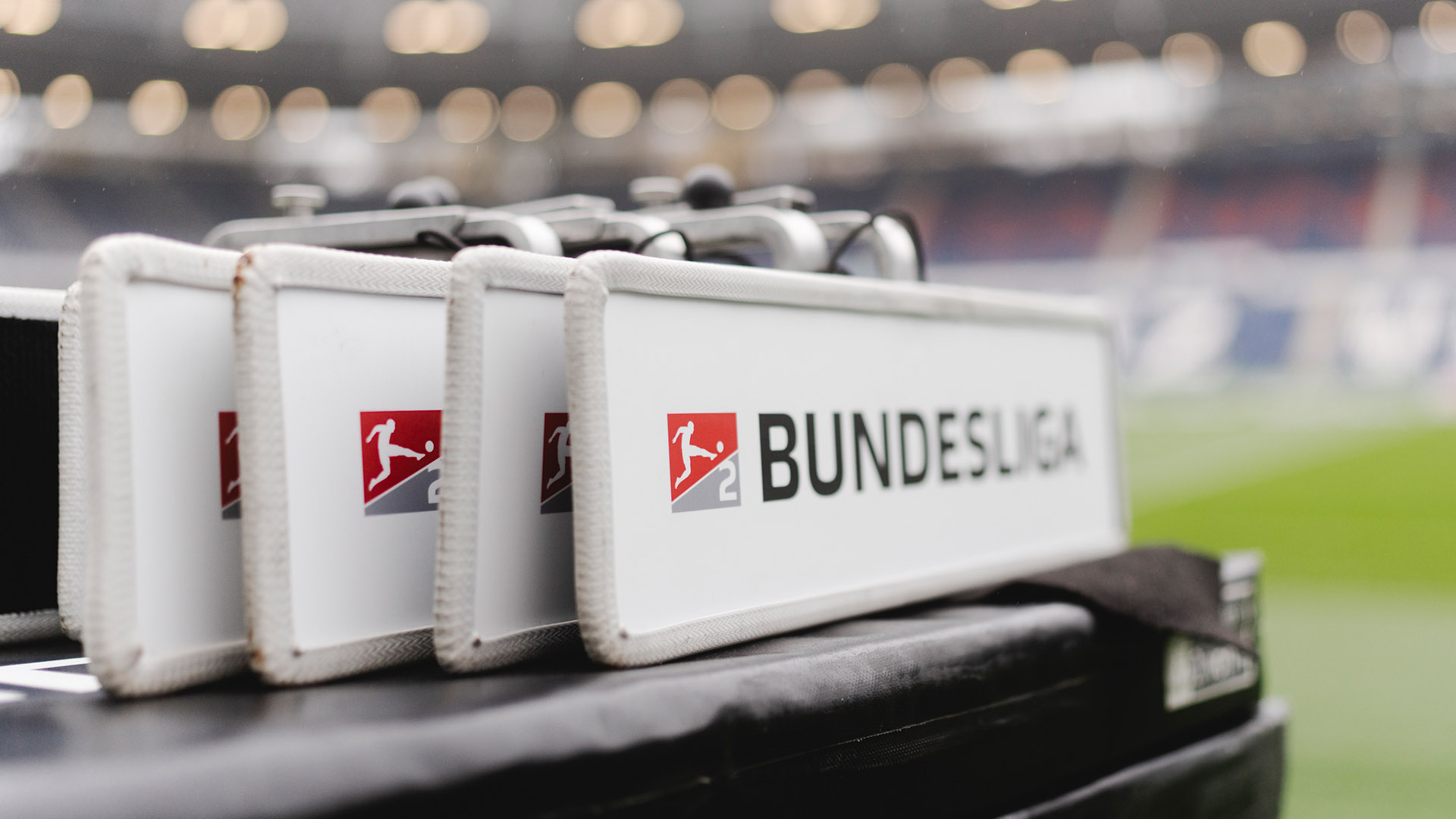 Mehrere Schilder mit dem Logo der 2. Bundesliga stehen hintereinander. Im unscharfen Hintergrund ist die Heinz von Heiden Arena zu sehen.