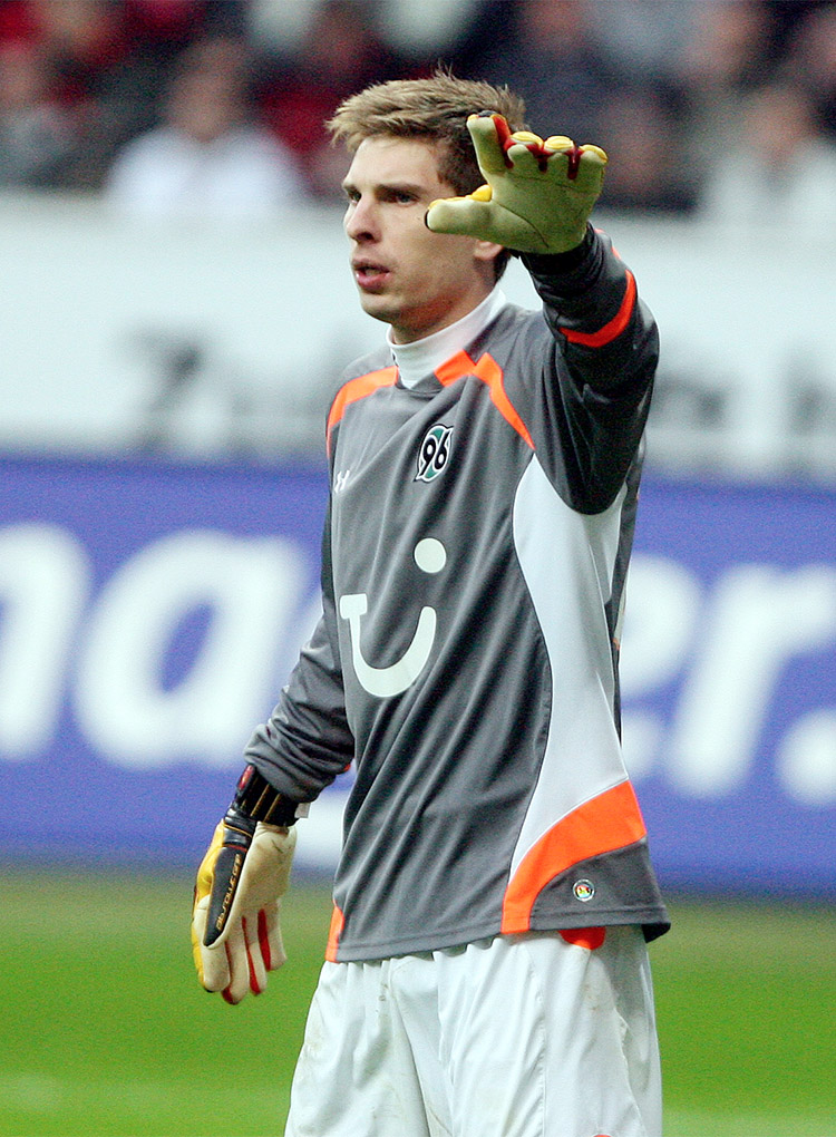 Ron-Robert Zieler in einem grauen Torwarttrikot deutet mit dem linken Arm nach links.  