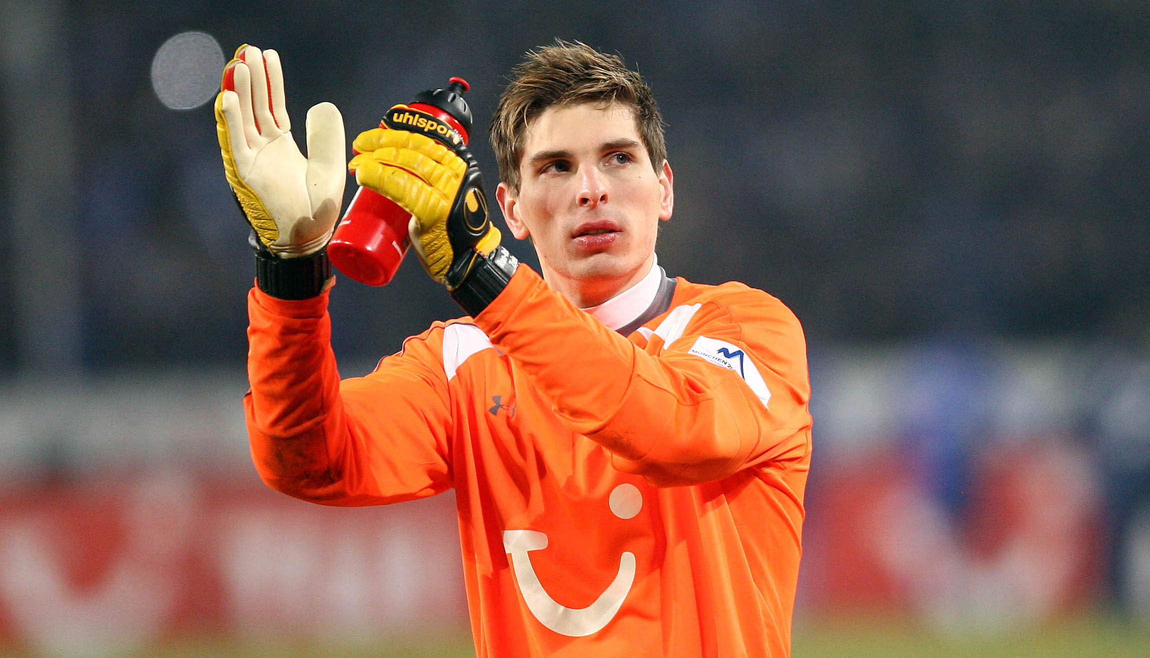 Ron-Robert Zieler in einem orangefarbenen Torwarttrikot klatscht.