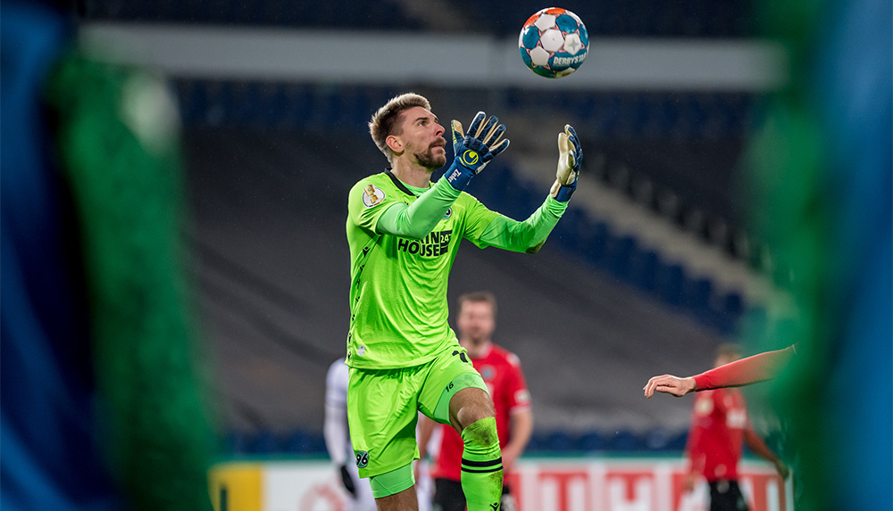 Ron-Robert Zieler im grünen Torwarttrikot springt in die Luft und fängt einen Ball.