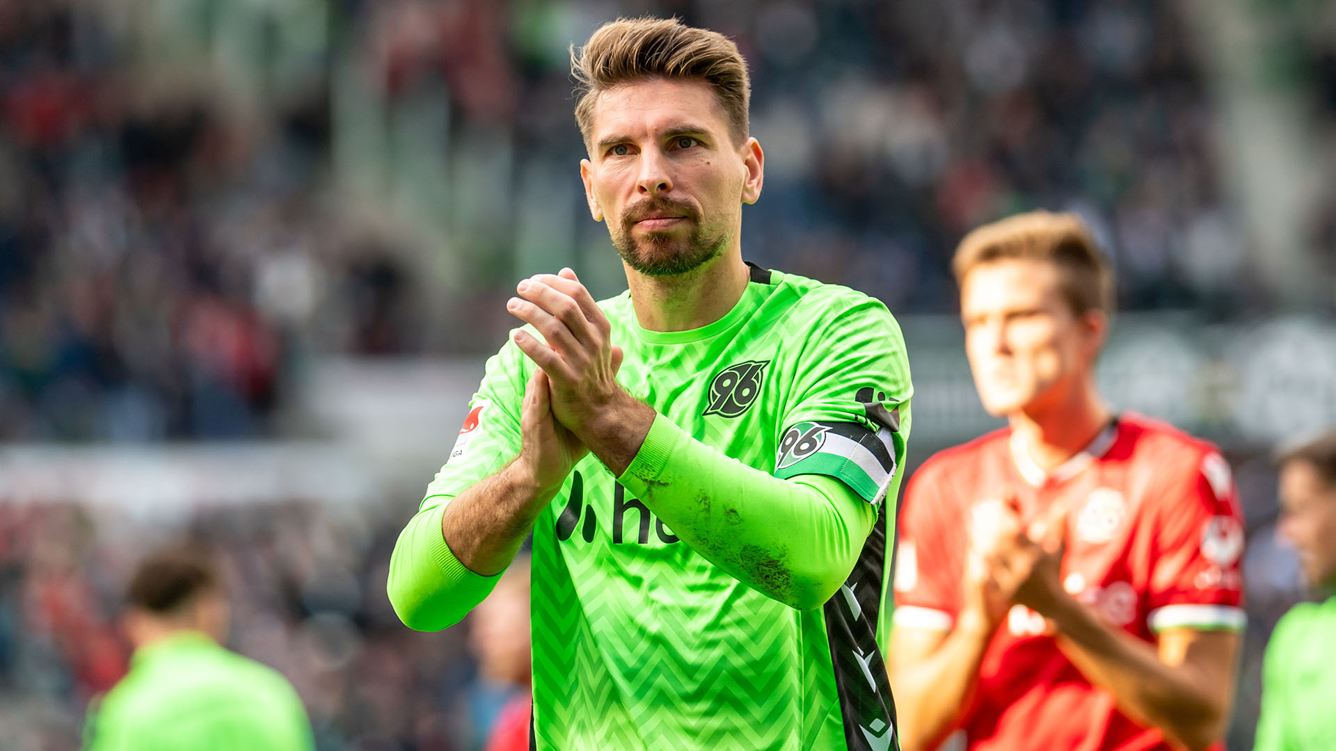 Ron-Robert Zieler hat die Hände vor der Brust, klatscht und blickt etwas nachdenklich in Richtung der Fans.