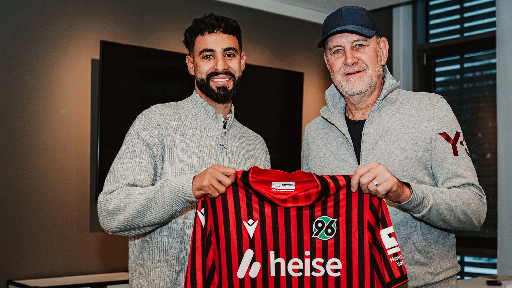 Elias Saad (links) und Jörg Schmadtke posieren mit dem 96-Heimtrikot.