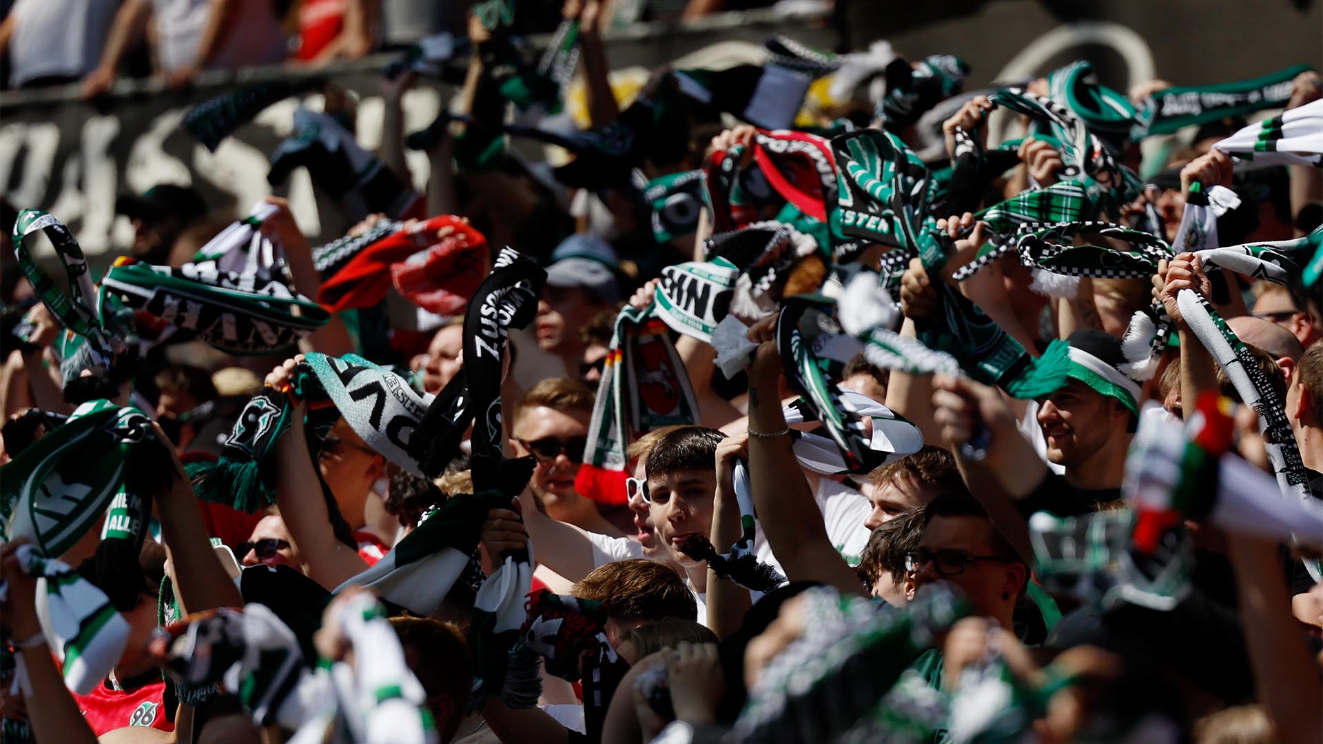 96-Fans im Stadion schwingen ihre Schals, die Sonne scheint.