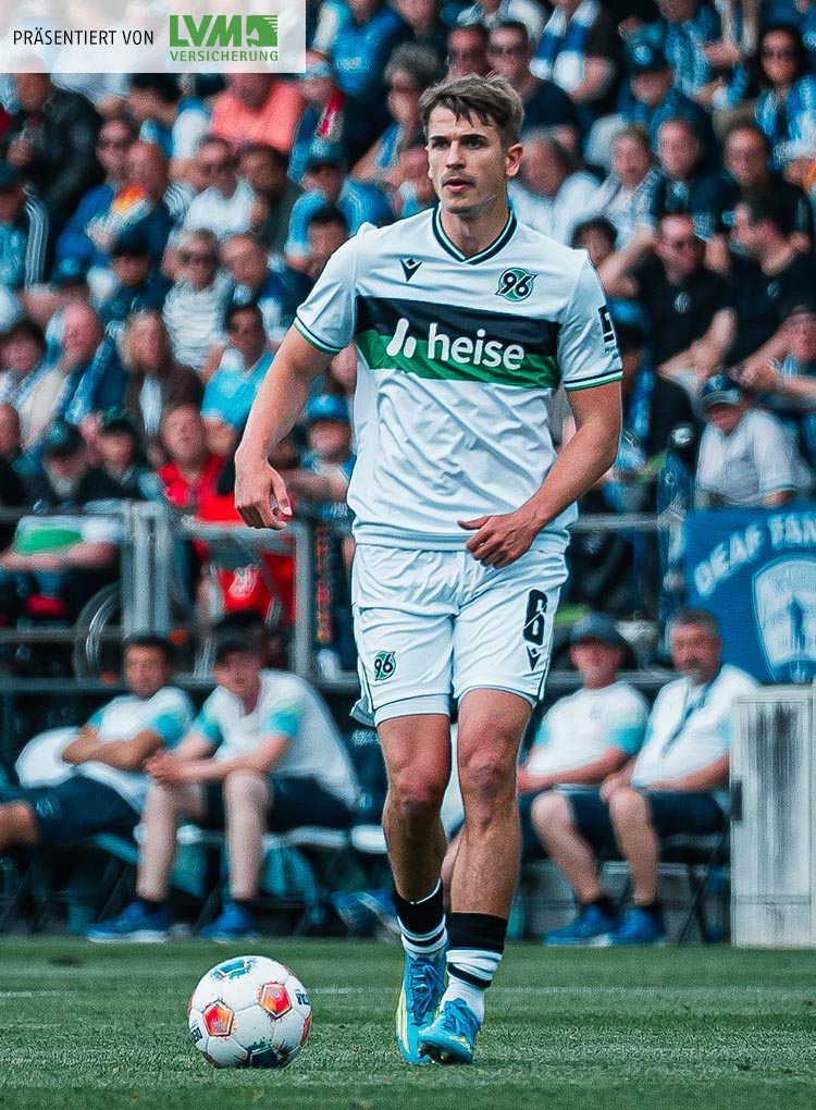 Maik Nawrocki im weißen Trikot am Ball, im Hintergrund unscharf Fans.