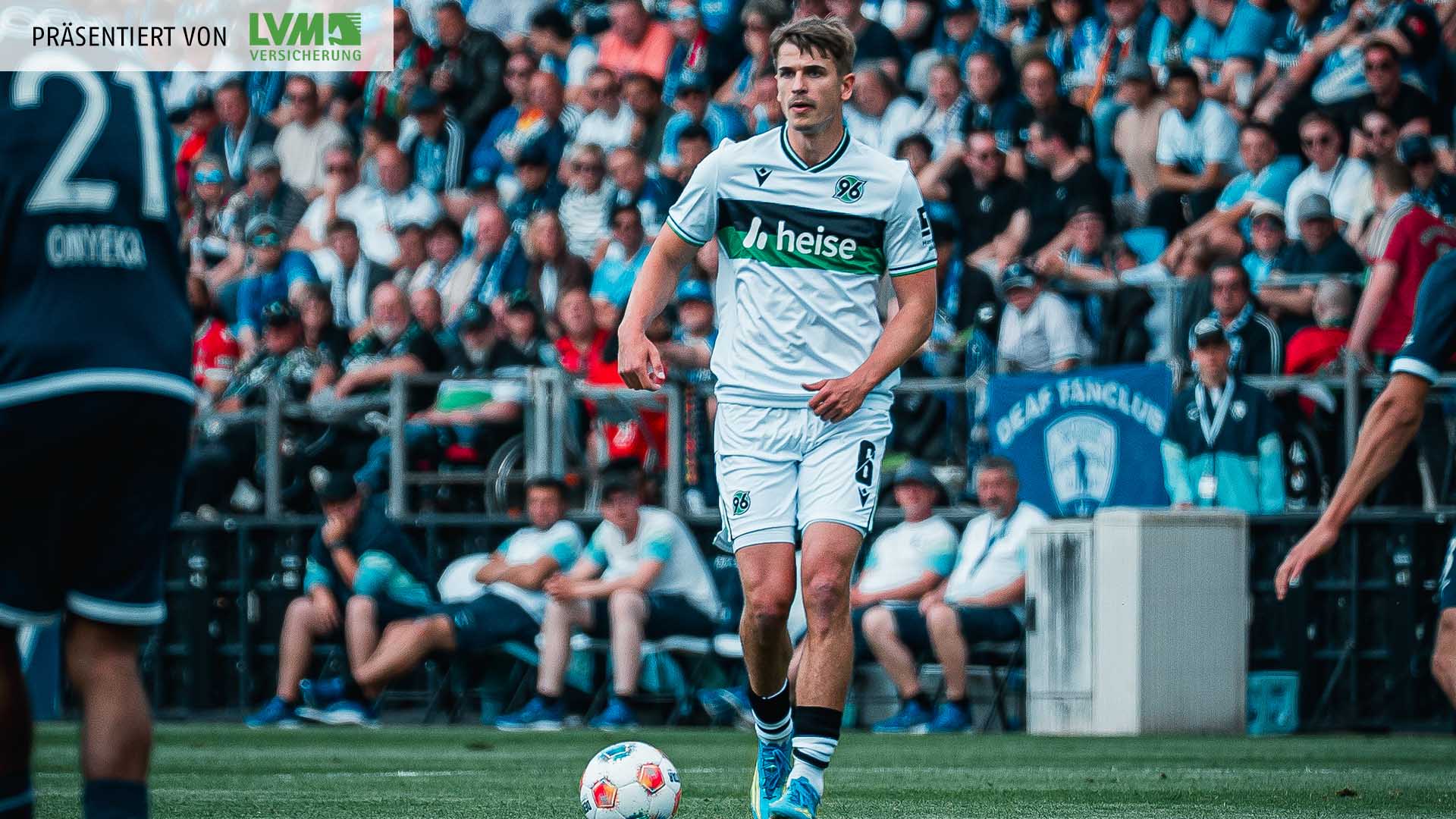 Maik Nawrocki im weißen Trikot am Ball, im Hintergrund unscharf Fans.