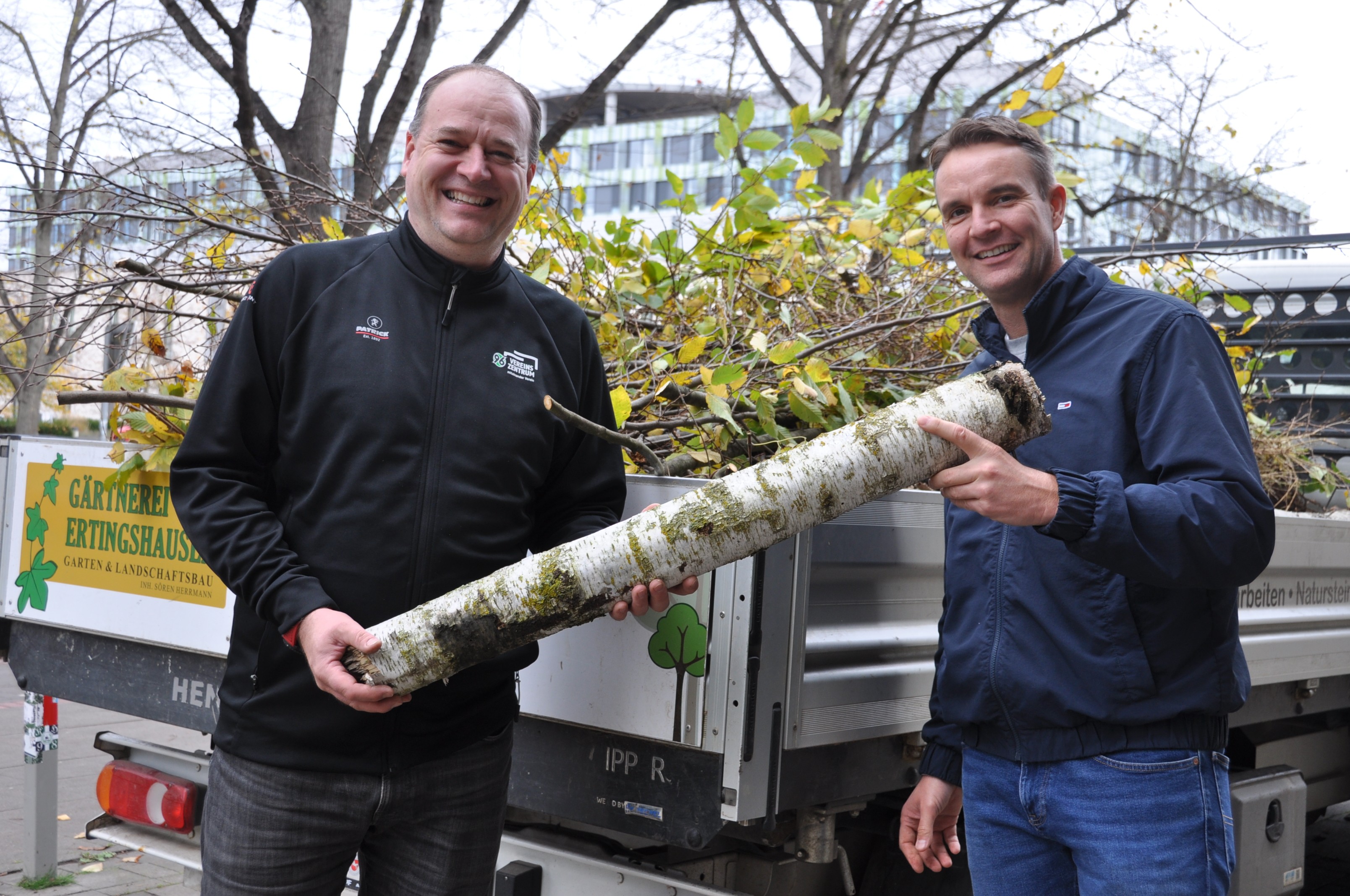 Sebastian Kramer und Björn Pollmann halten einen Baumstamm in der Hand.