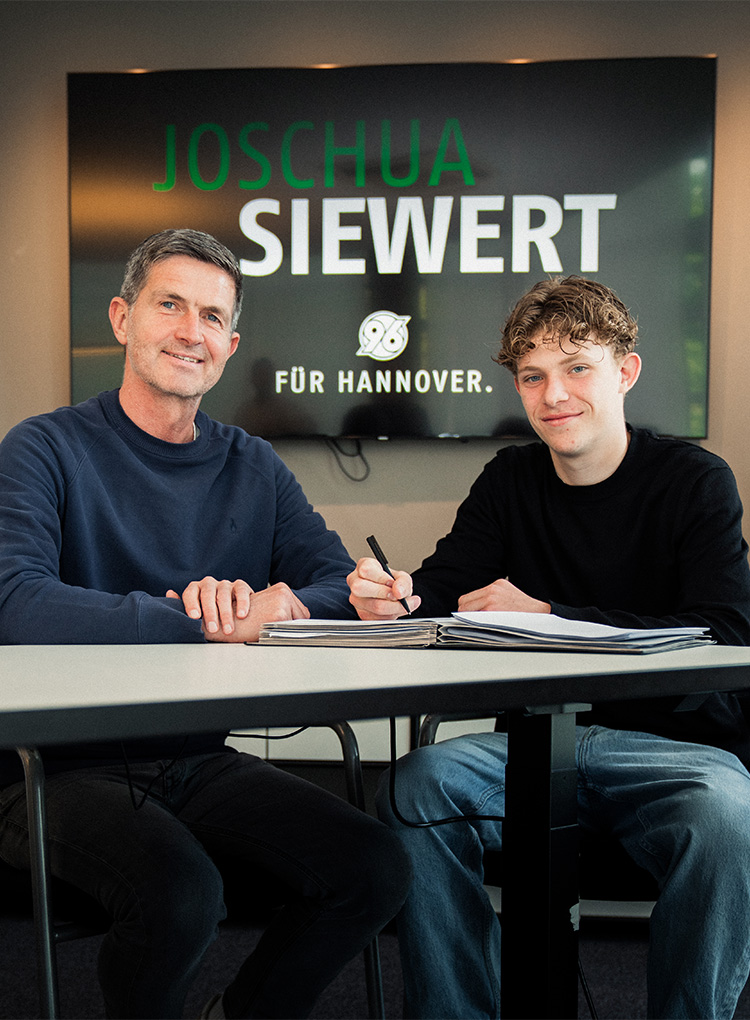 Joshua Siewert mit Ralf Becker bei der Unterschrift, im Hintergrund ein Bildschirm, auf dem groß sein Name steht.