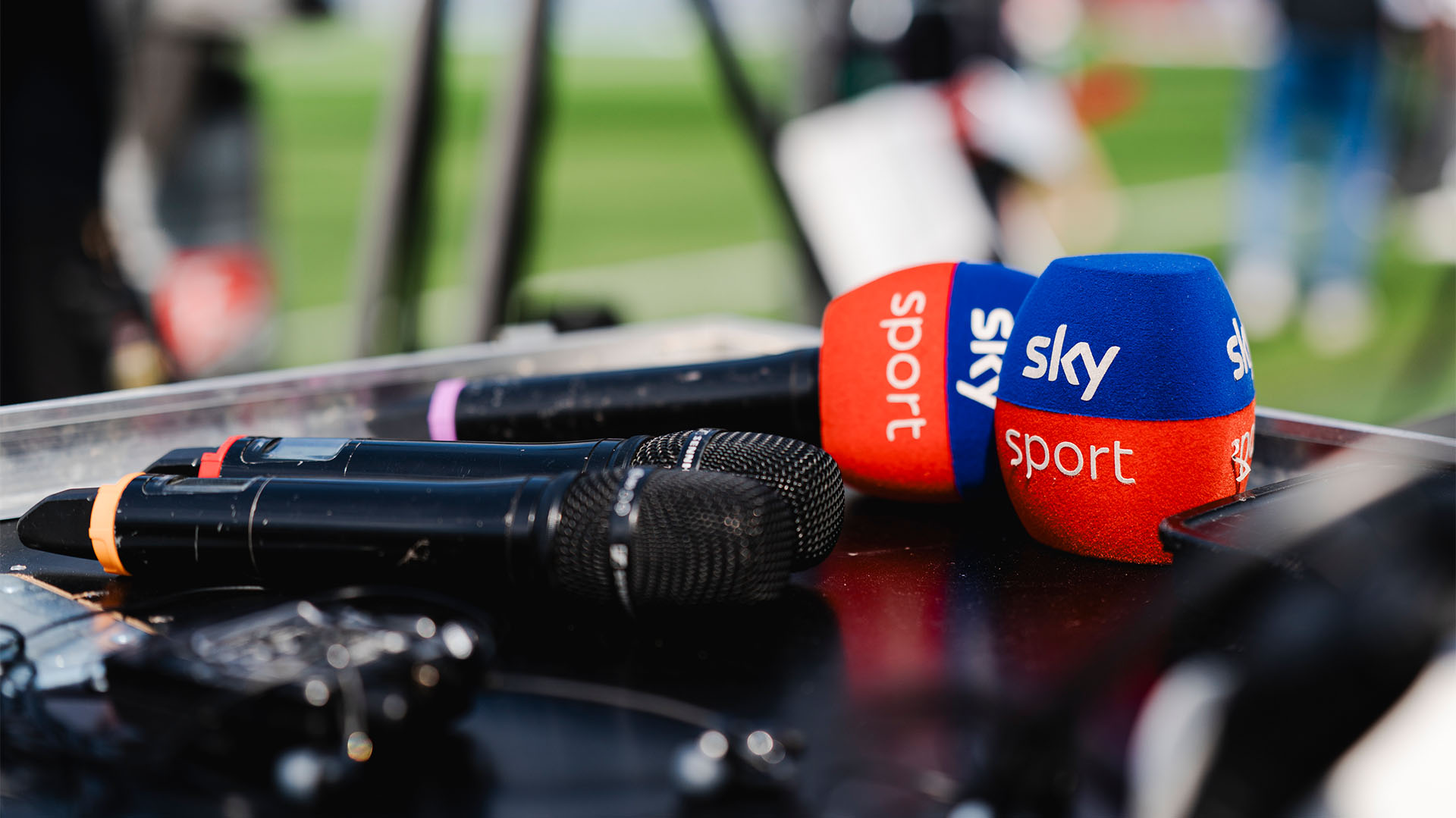 Drei Mikrofone liegen auf einem Tisch, eines hat einen Sky-Sport-Schutz, ein Schutz liegt daneben.