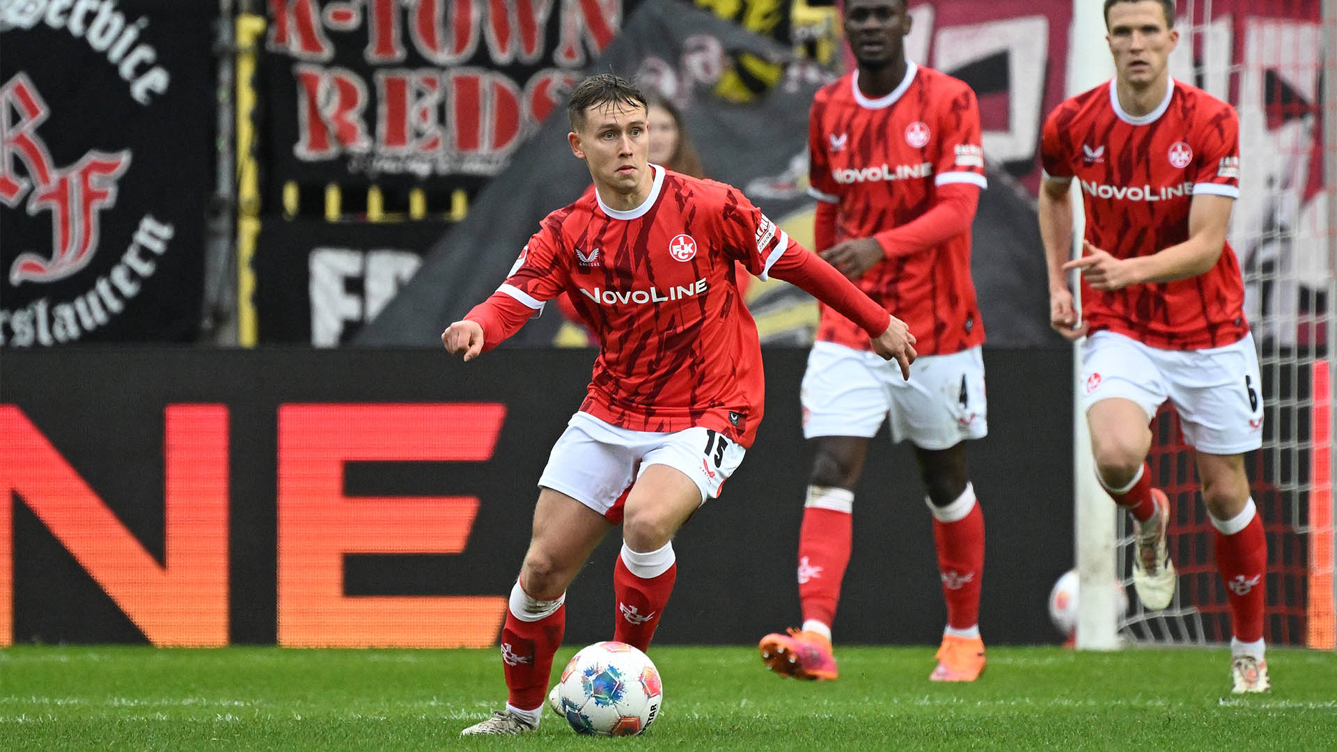 Naatan Skyttä im roten Trikot und weißer Hose mit dem Ball an seinem linken Fuß. Im Hintergrund ist einer seiner Mitspieler unscharf zu erkennen.