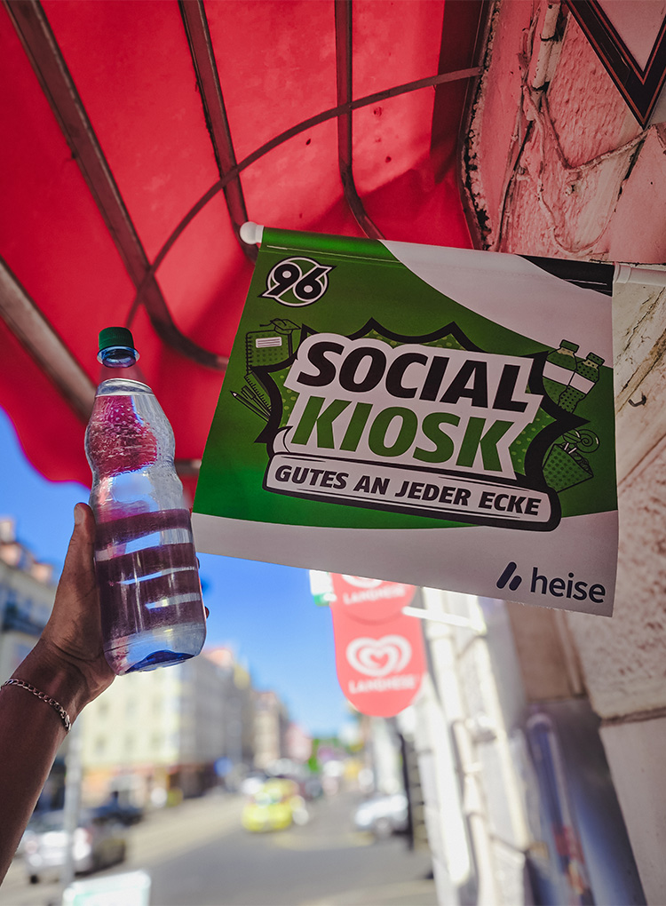 Neben einer SOCIAL-KIOSK-Fahne mit der Aufschrift "Gutes an jeder Ecke" wird eine Wasserflasche hochgehalten.