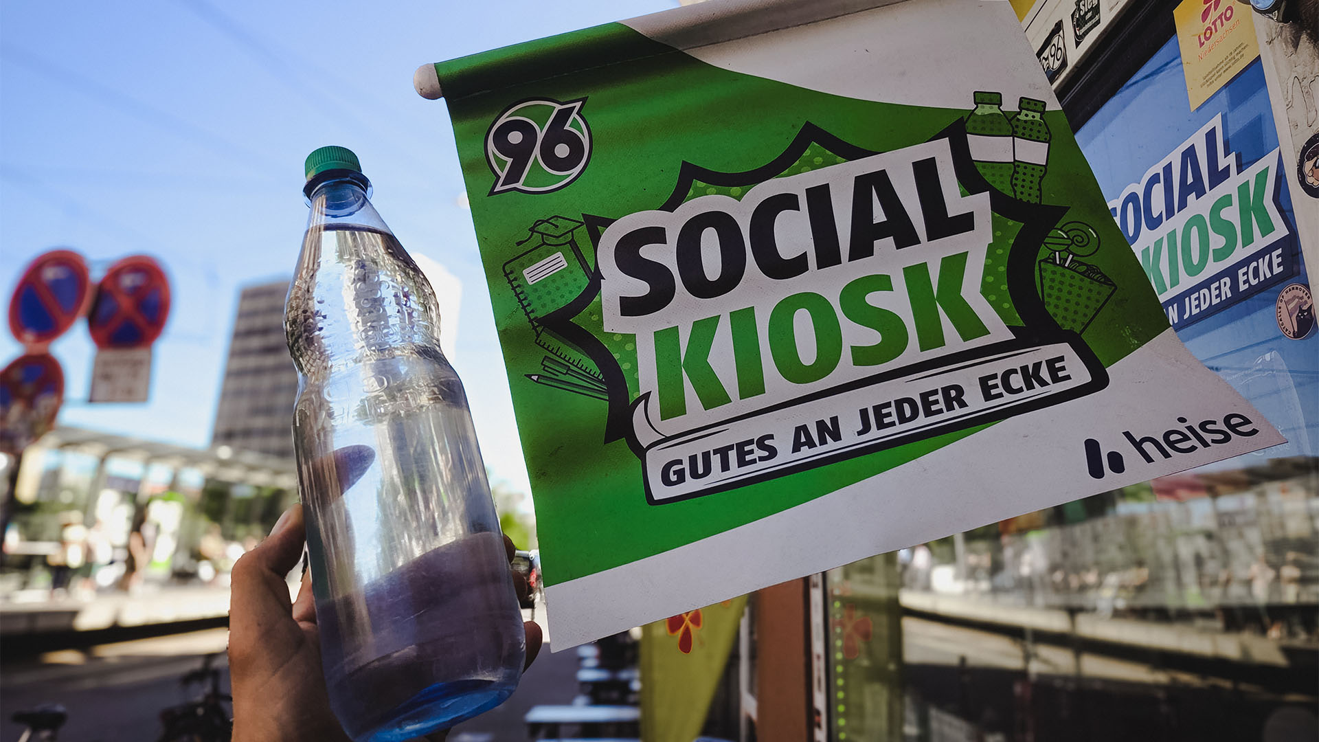 Neben einer SOCIAL-KIOSK-Fahne mit der Aufschrift "Gutes an jeder Ecke" wird eine Wasserflasche hochgehalten.
