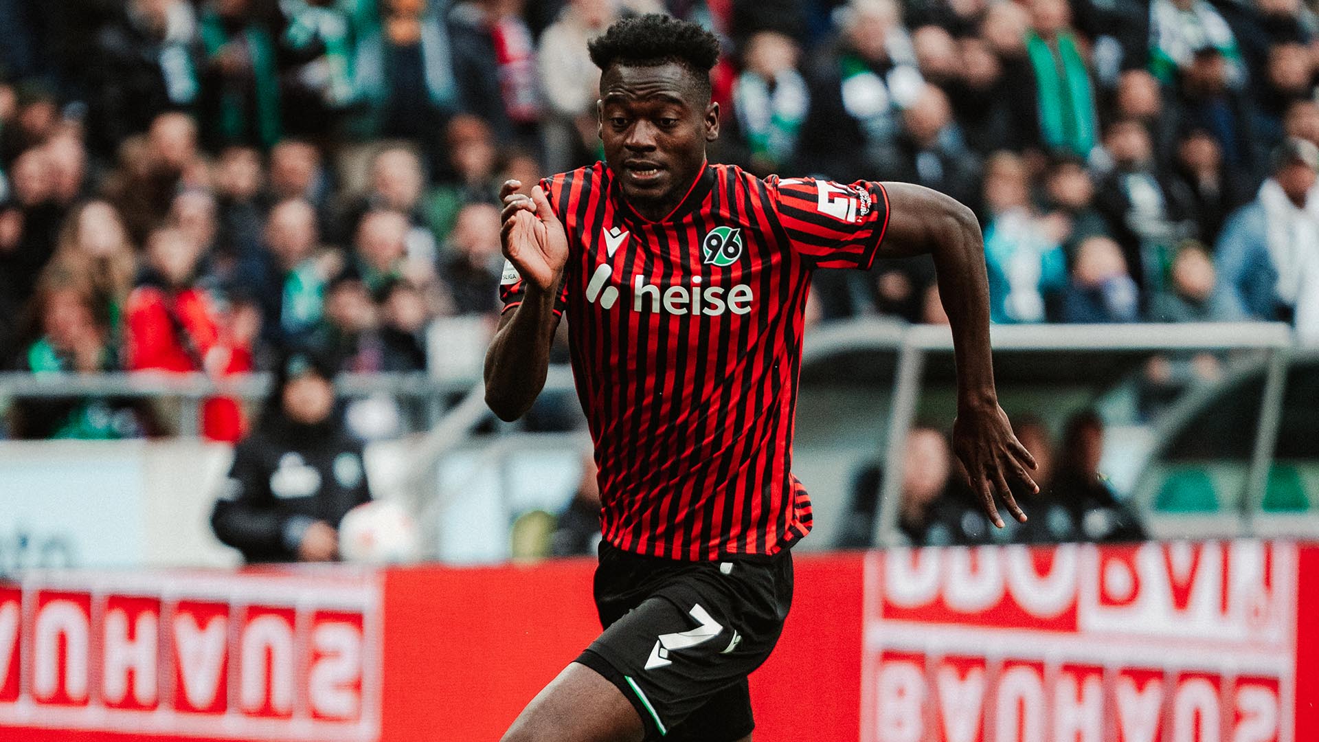 Mustapha Bundu im Heimtrikot am Ball, dahinter volle Ränge.