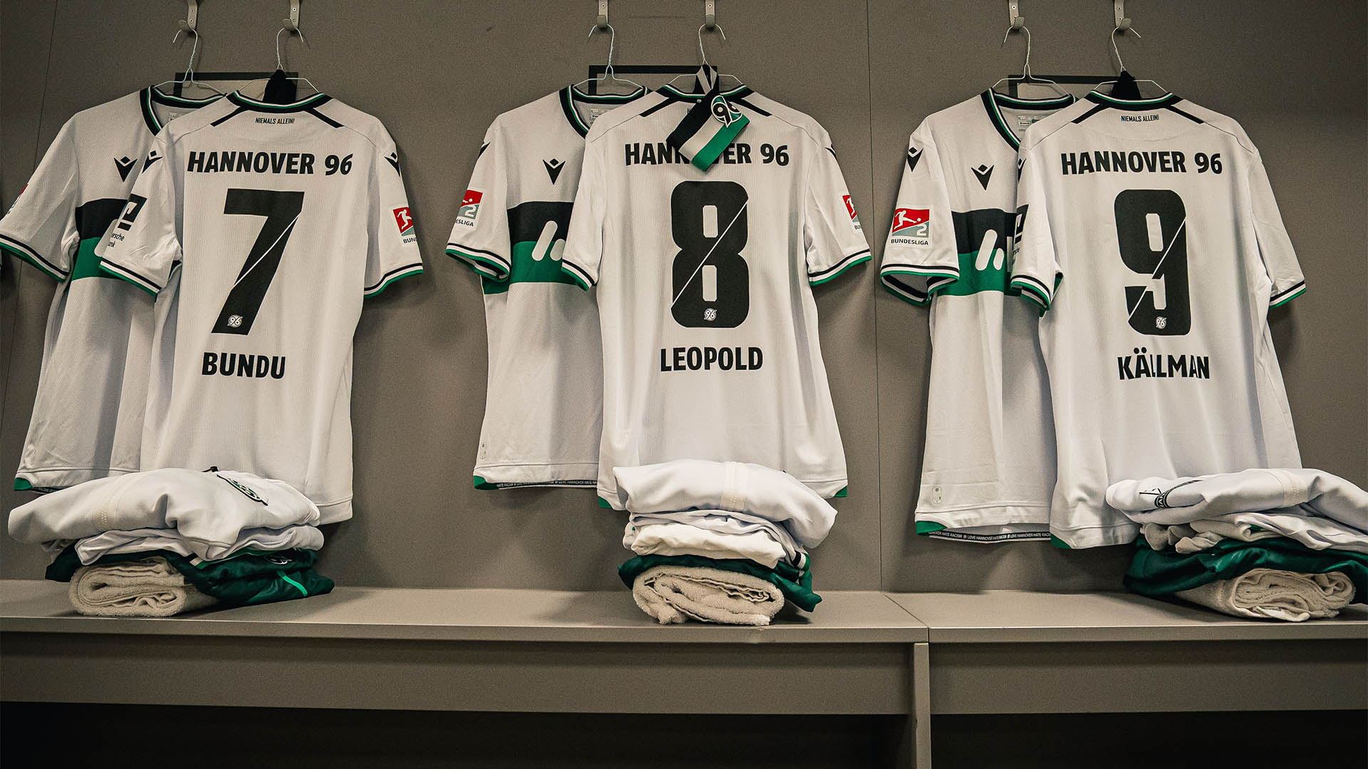 Drei weiße 96-Trikots hängen in der Kabine.