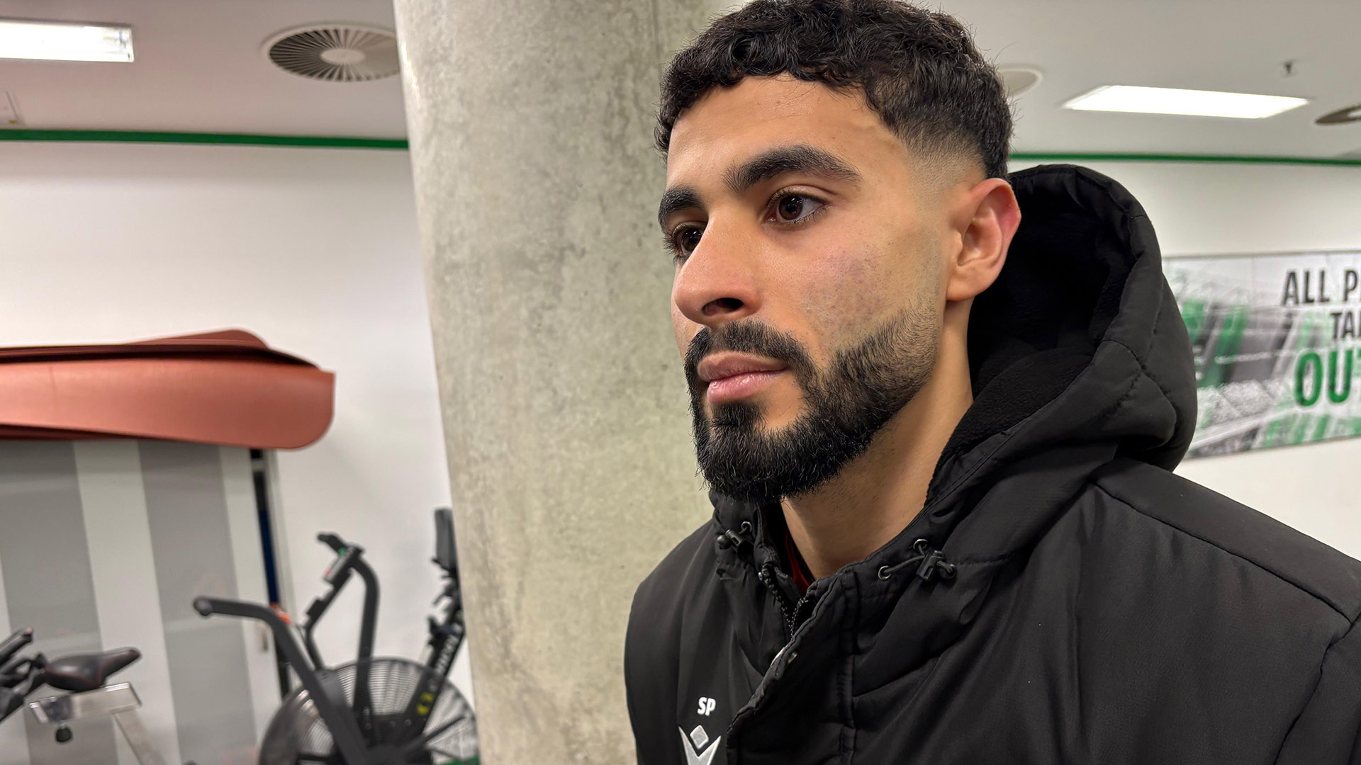 Elias Saad in 96-Jacke in den Innenräumen der Arena.