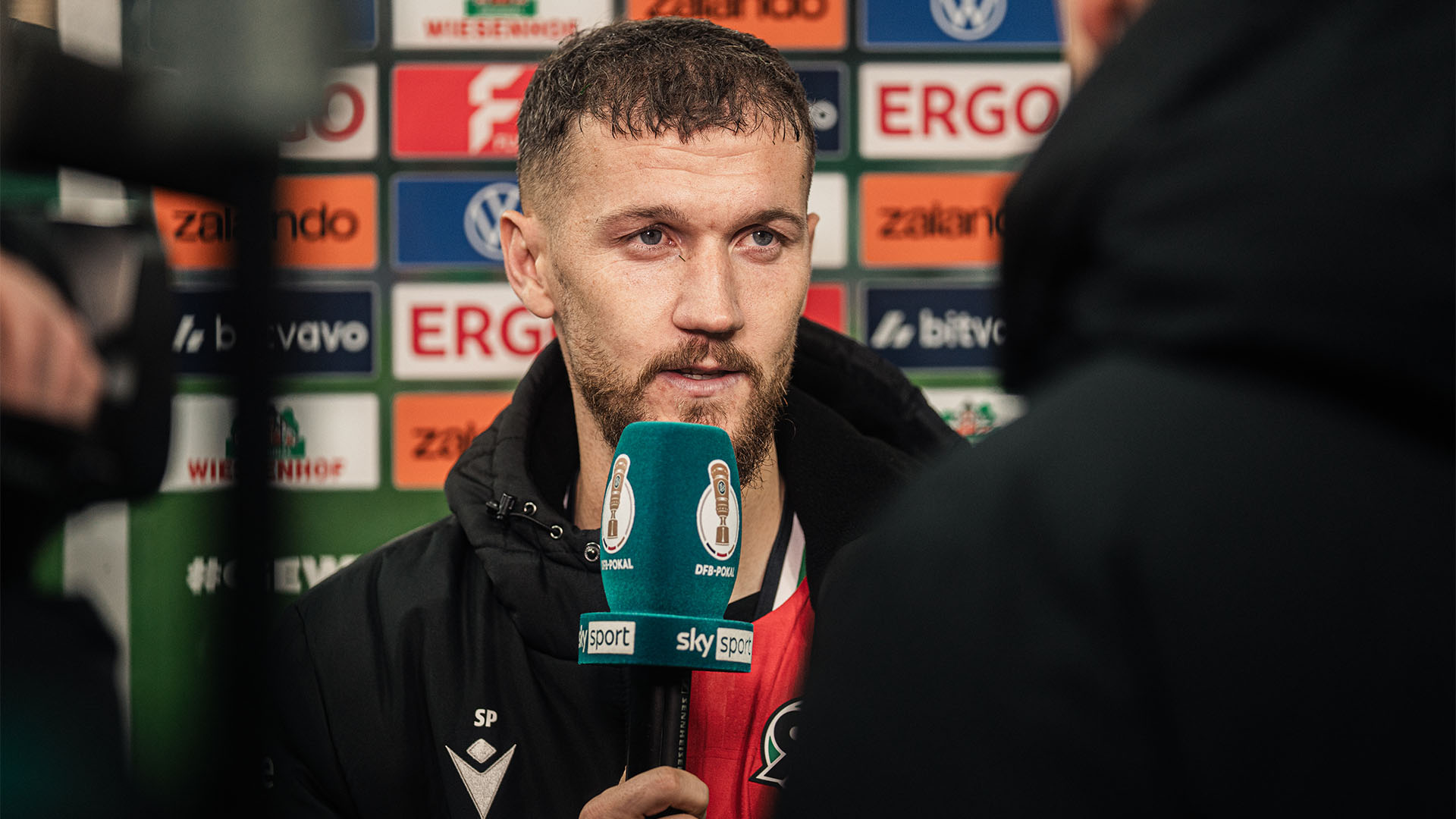 Der 96-Spieler Marcel Hartel im Heimtrikot und mit Jacke am Sky-Mikrofon.