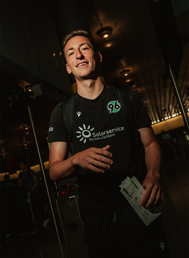Marius Wörl lächelt am Flughafen in die Kamera, er hält eine Boardkarte in der Hand.
