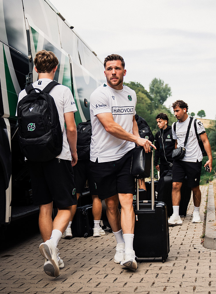 Mehrere Spieler steigen aus dem Bus aus und laden Gepäck aus.