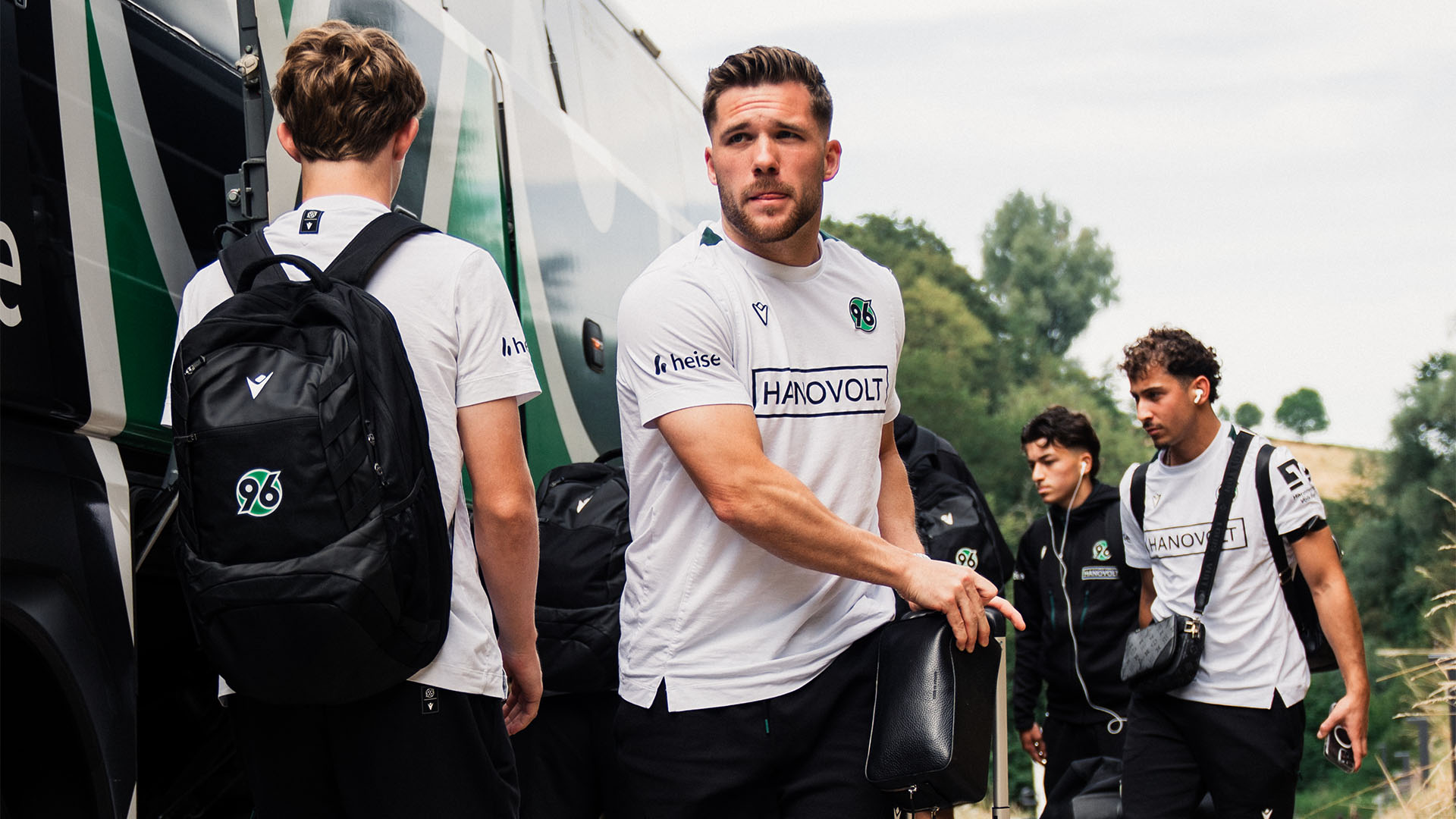 Mehrere Spieler steigen aus dem Bus aus und laden Gepäck aus.