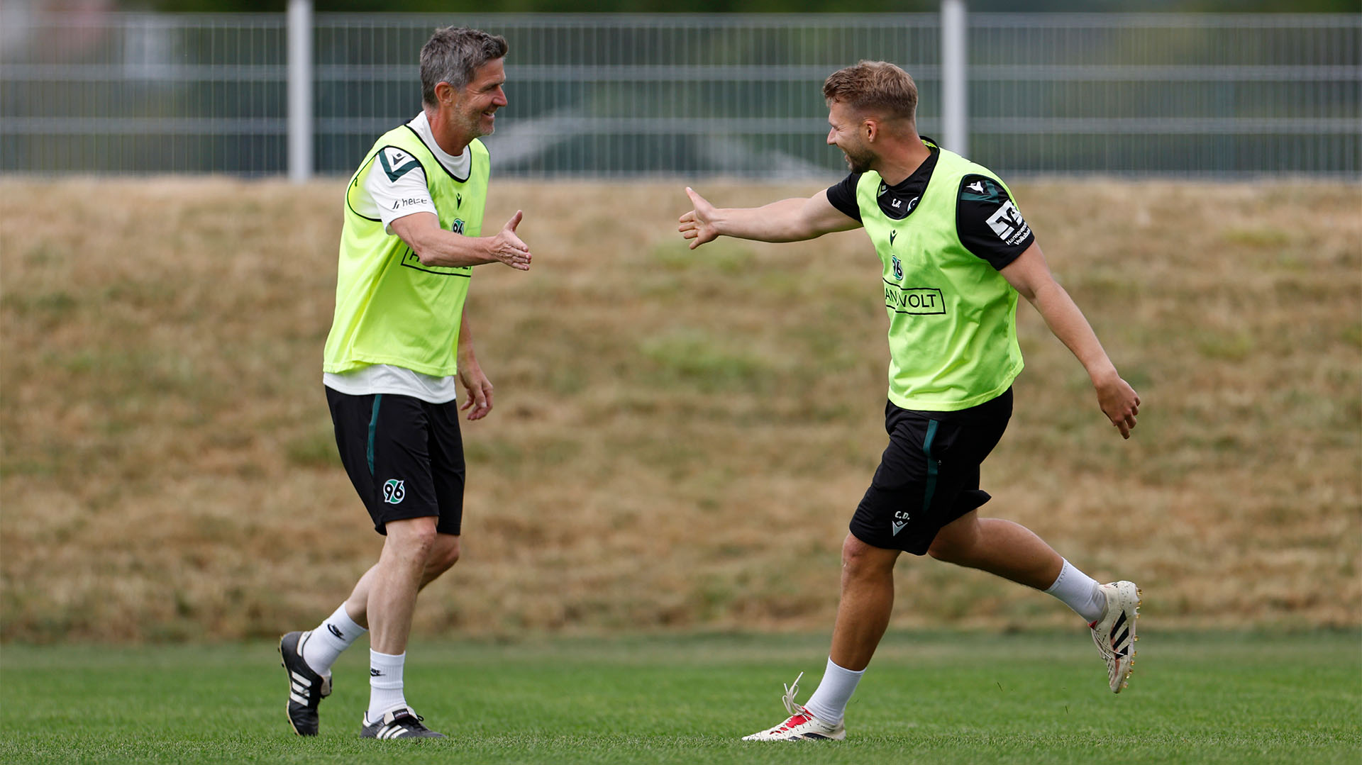 Zwei Männer in Trainingskleidung und mit Leibchen klatschen miteinander ab.