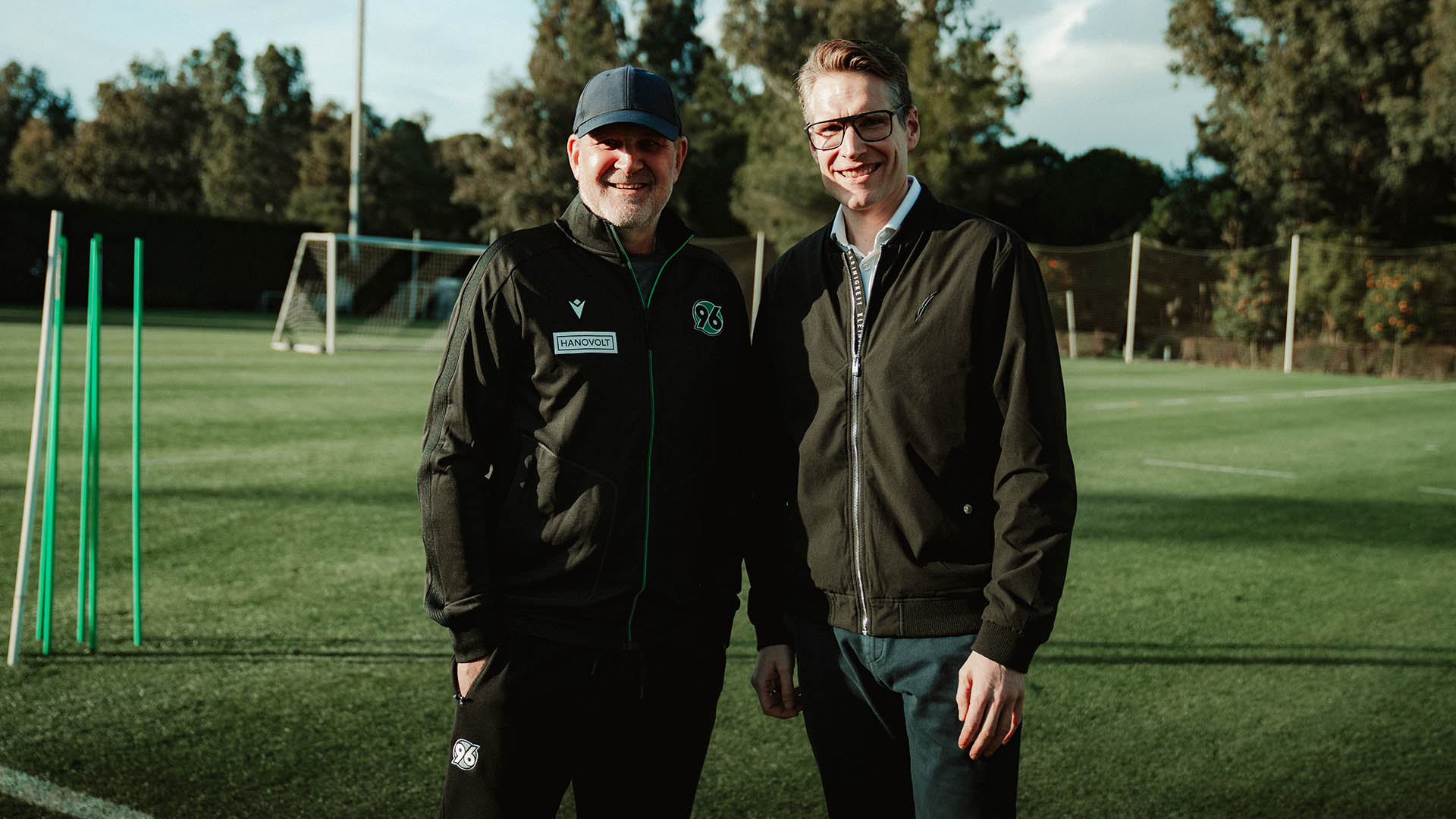 Jörg Schmadtke und Henning Bindzus stehen nebeneinander auf dem Trainingsplatz in Belek.  