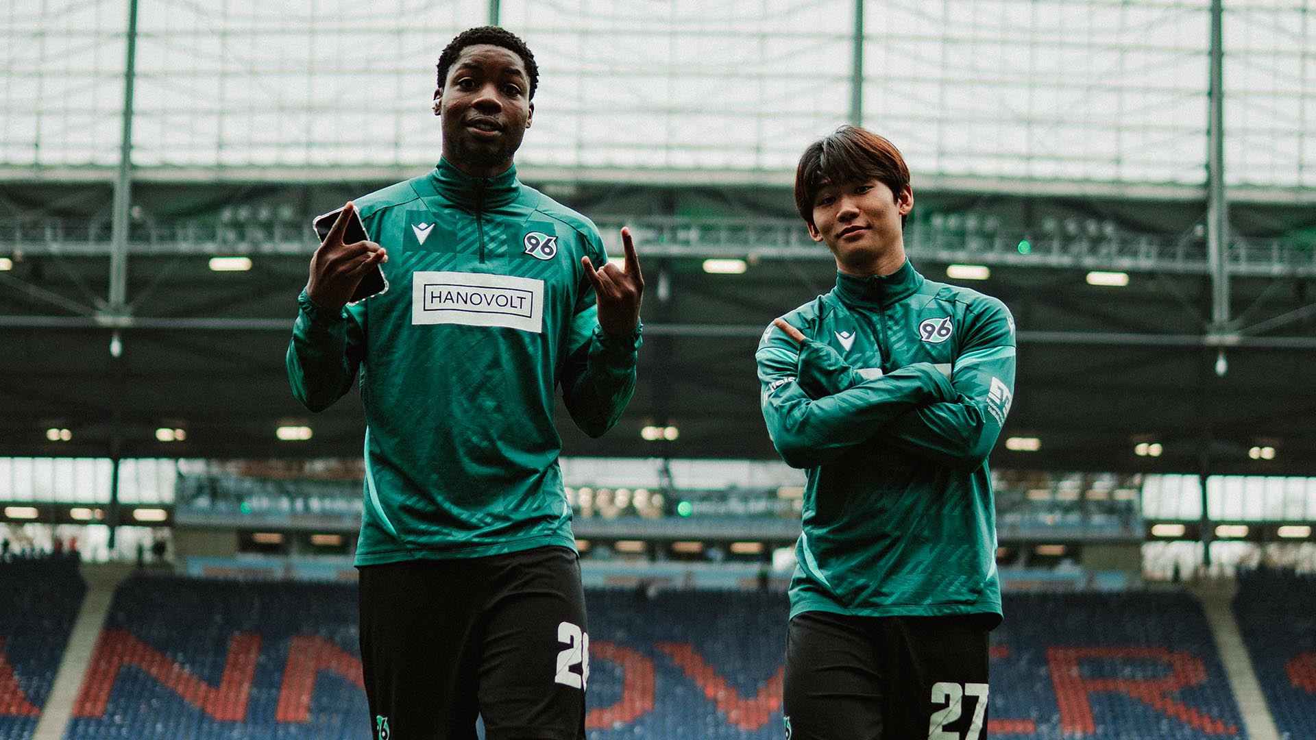 Ime Okon und Hayate Matsude stehen in Trainingskleidung im leeren Stadion.