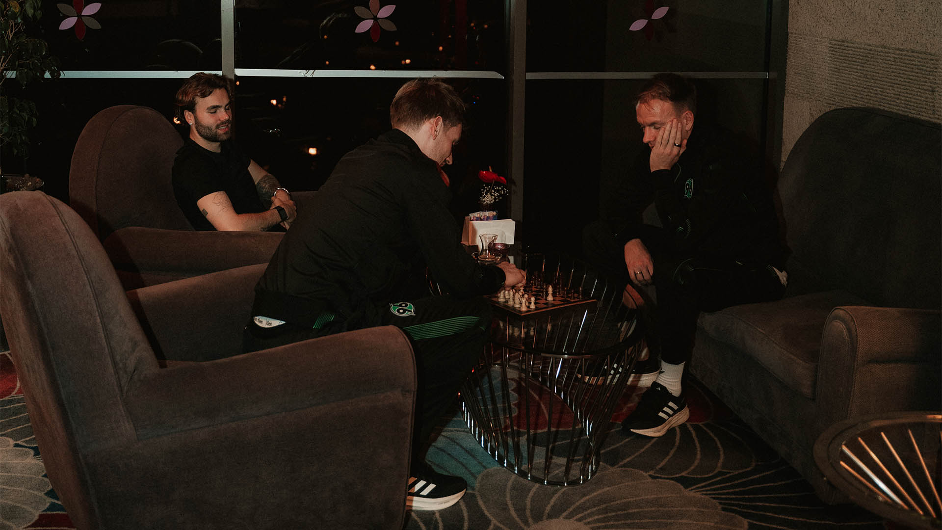 Kolja Oudenne, Leo Weinkauf und Havard Nielsen sitzen in einer Sofaecke im Hotel und spielen Schach. 