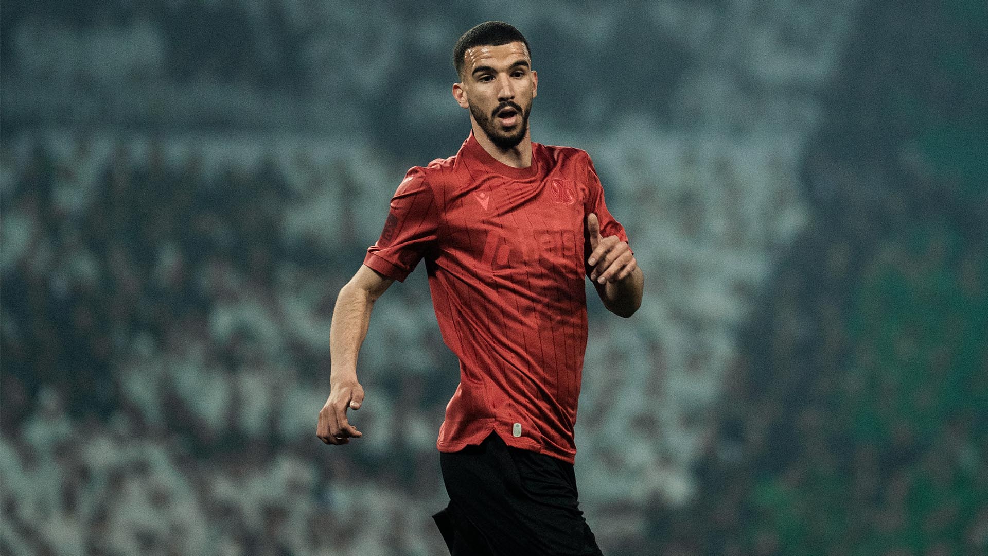 Waniss Taibi läuft im Jubiläumstrikot, im Hintergrund eine schwarz-weiß-grüne Choreo. 