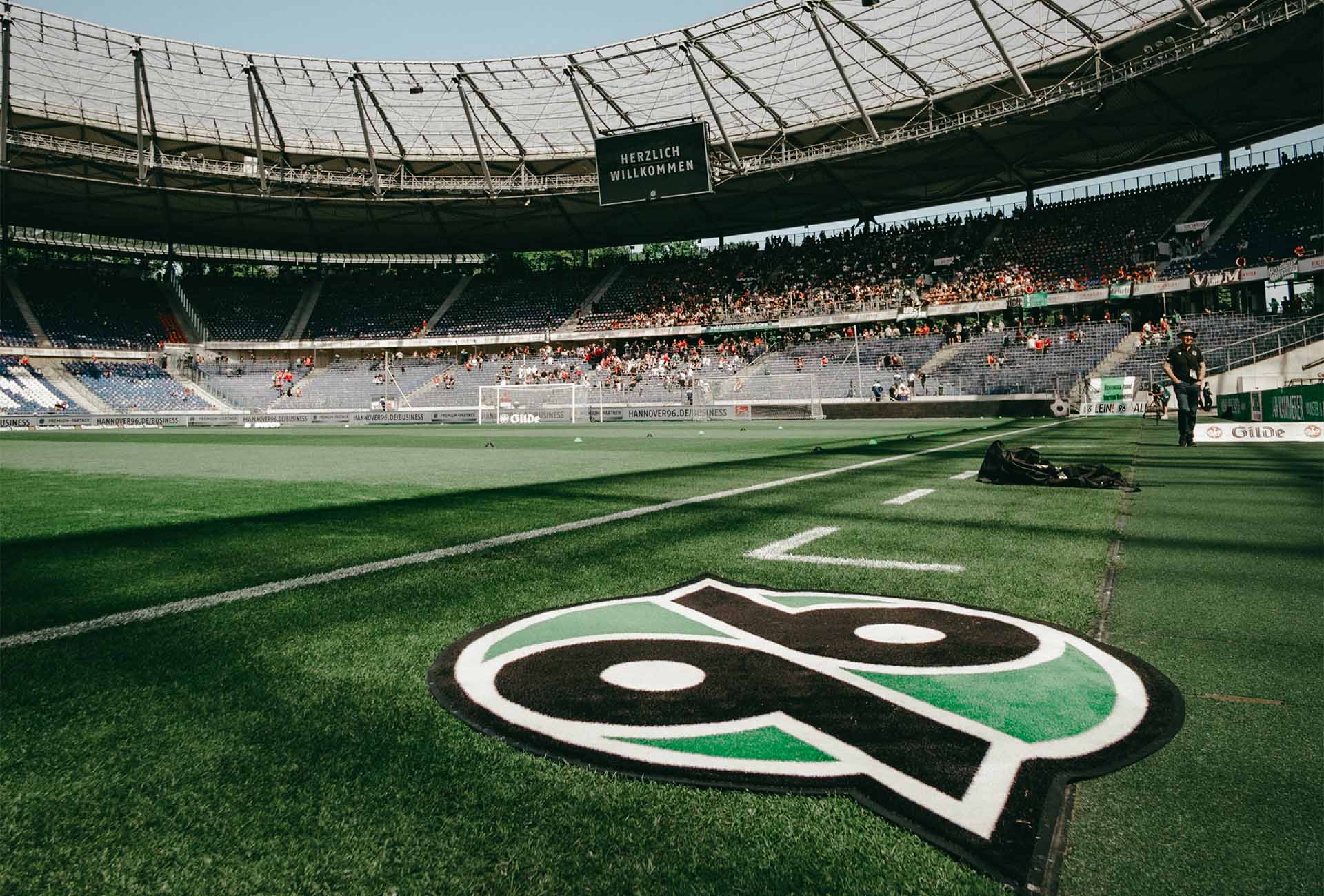 Das 96-Logo liegt als Teppich in der Heinz von Heiden Arena, im Hintergrund ist die leicht gefüllte Nordkurve zu sehen. 