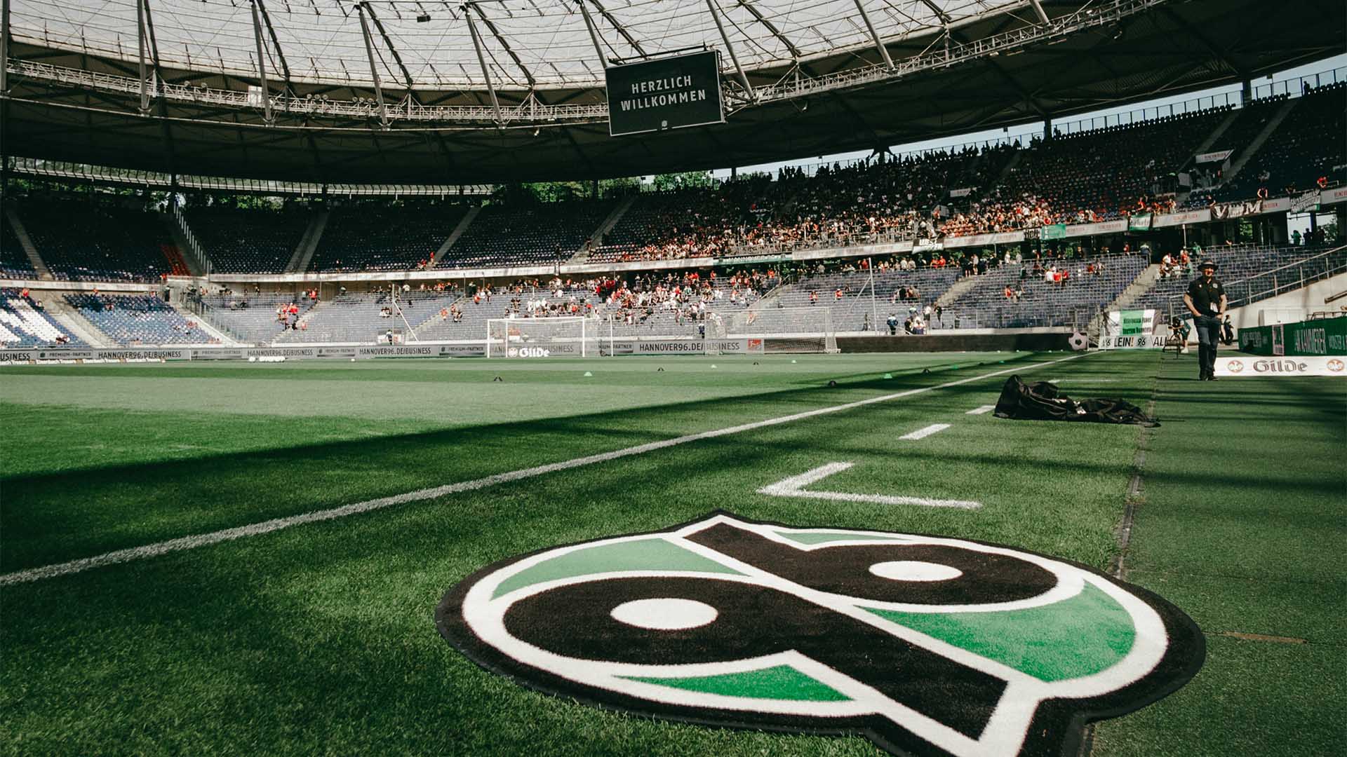 Das 96-Logo liegt als Teppich in der Heinz von Heiden Arena, im Hintergrund ist die leicht gefüllte Nordkurve zu sehen. 