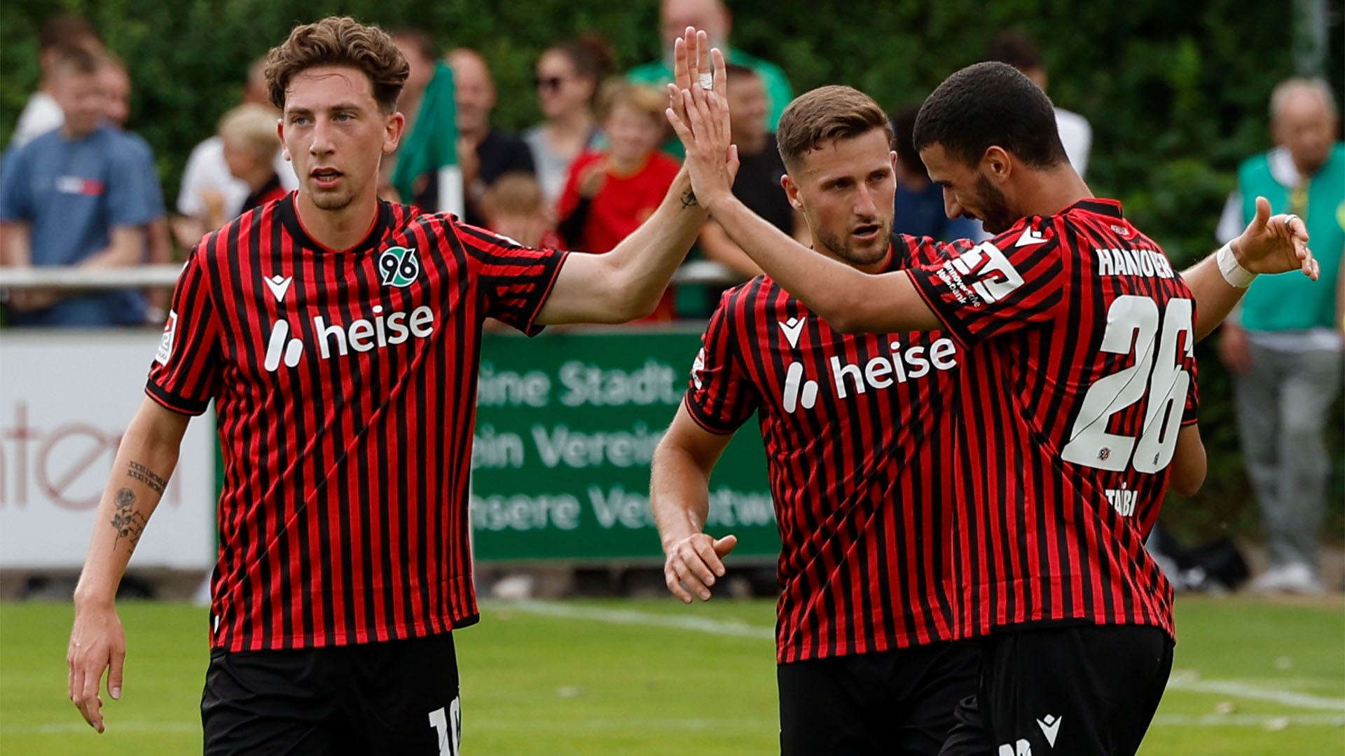 Jannik Rochelt und Waniss Taibi klatschen ab, dahinter steht Enzo Leopold, im Hintergrund unscharf ein paar Fans. 