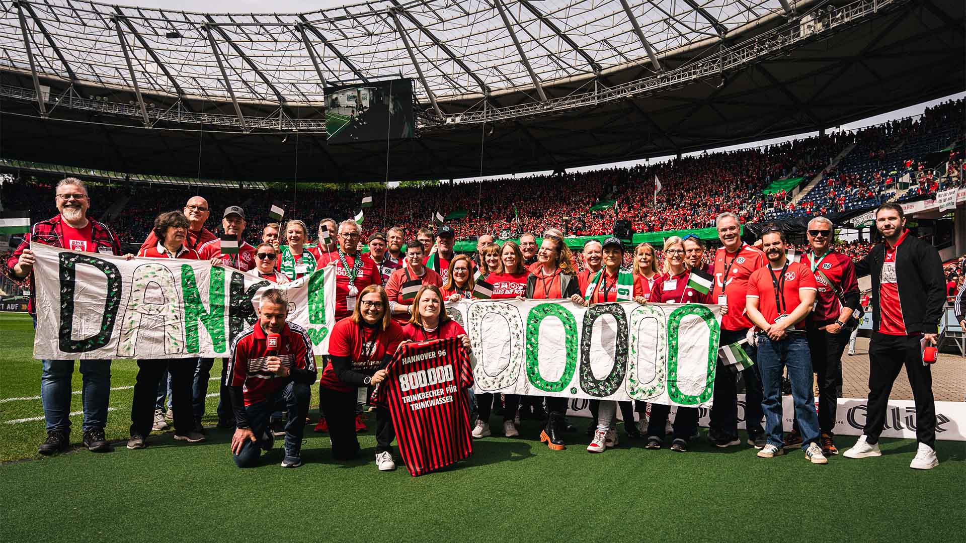 Eine Gruppe von Menschen steht im vollen Stadion, sie halten Banner mit "Danke" und "800.000".