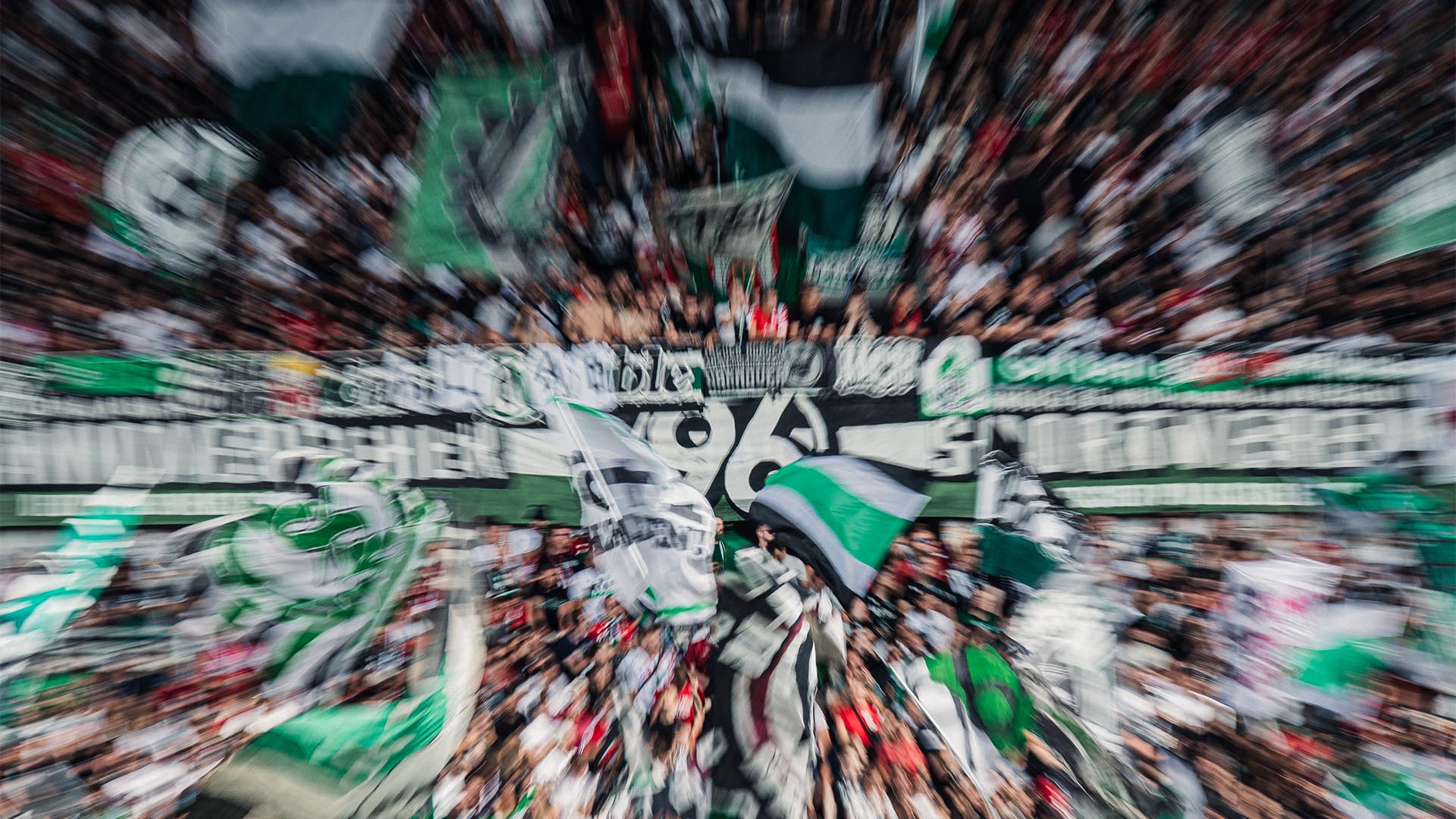 Unscharfes Bild einer Fankurve mit 96-Fans mit 96-Fahnen.