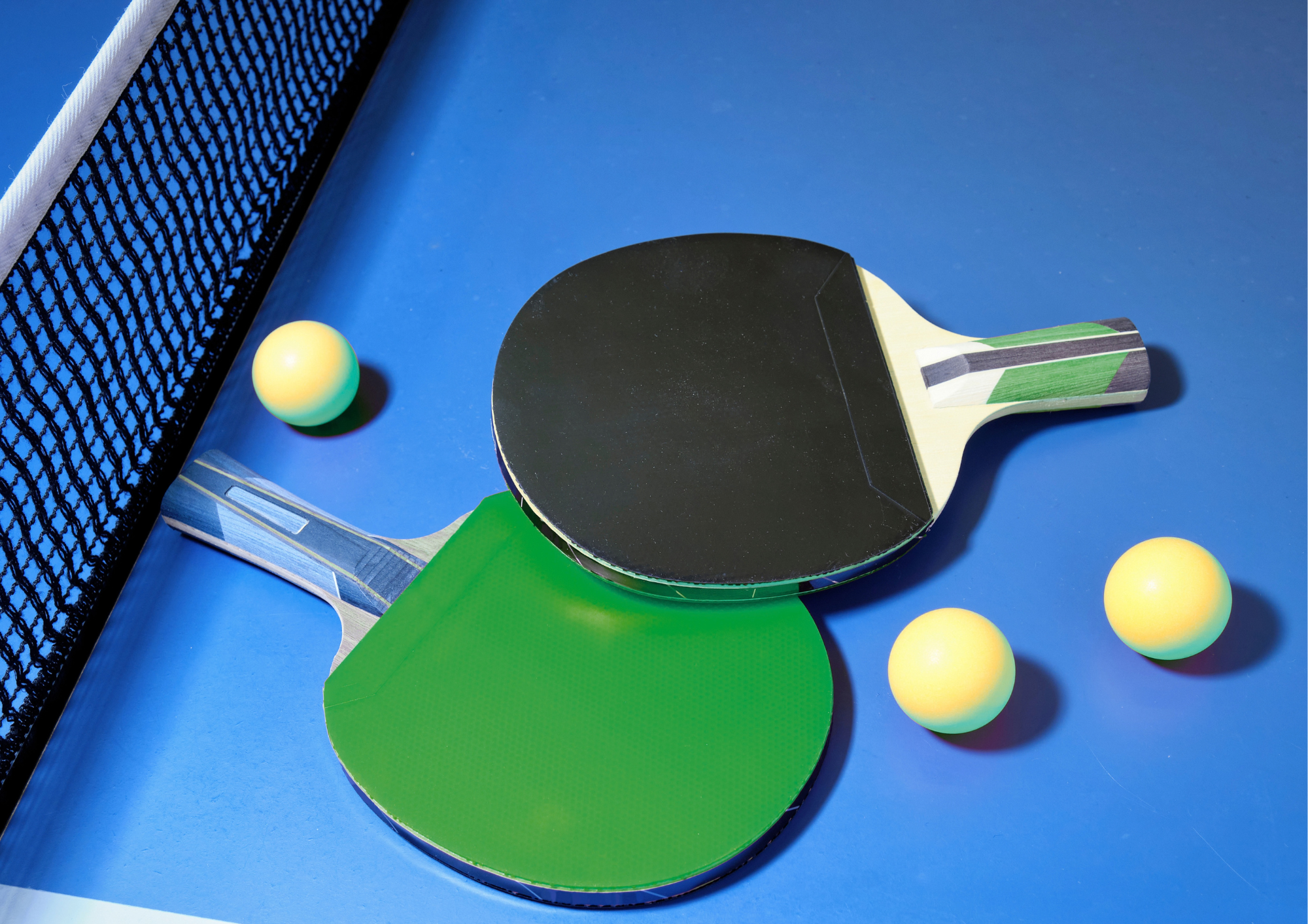 Zwei Tischtennisschläger und drei Bälle auf einer Platte.