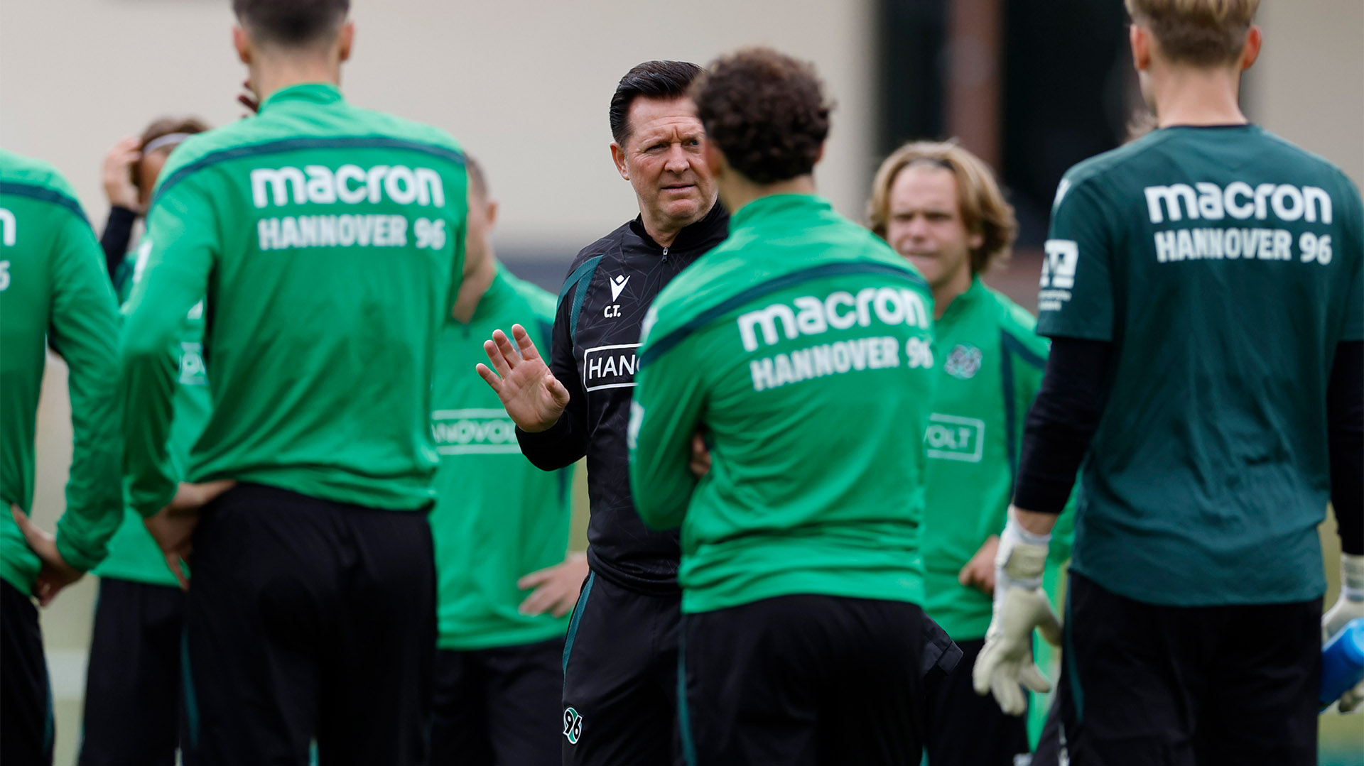 96-Cheftrainer Christian Titz spricht mit Spielern, die unscharf von hinten zu sehen sind.