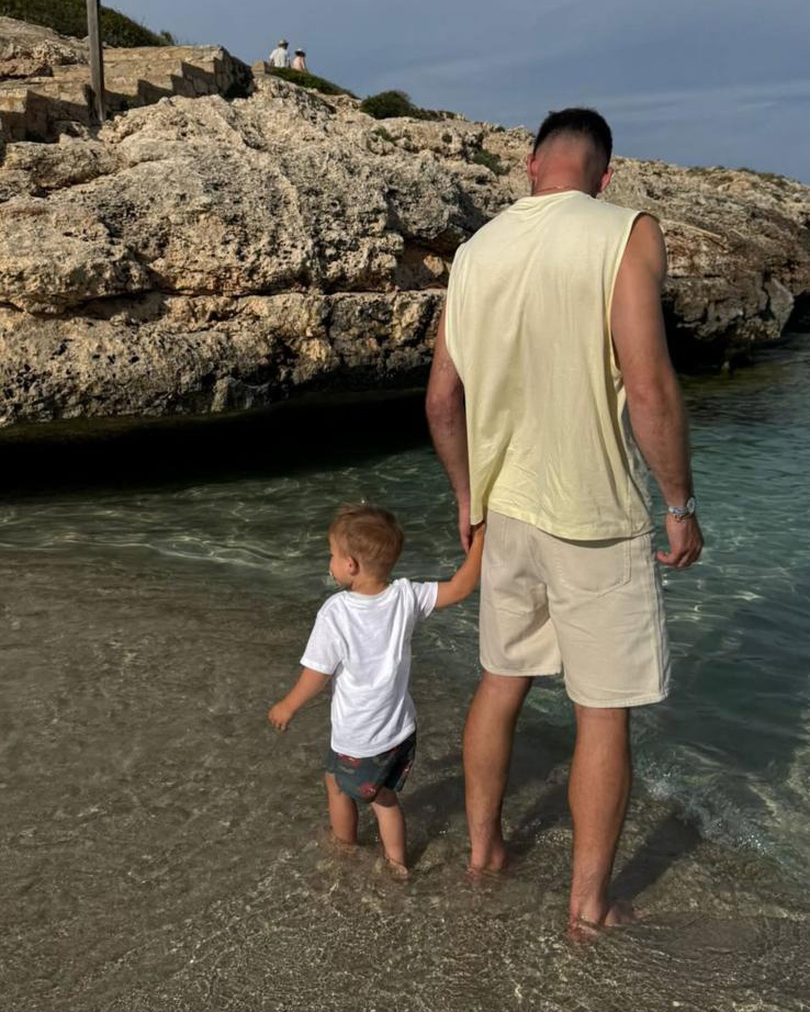 Boris und sein Sohn stehen mit den Füßen im Wasser und schauen auf das Meer.