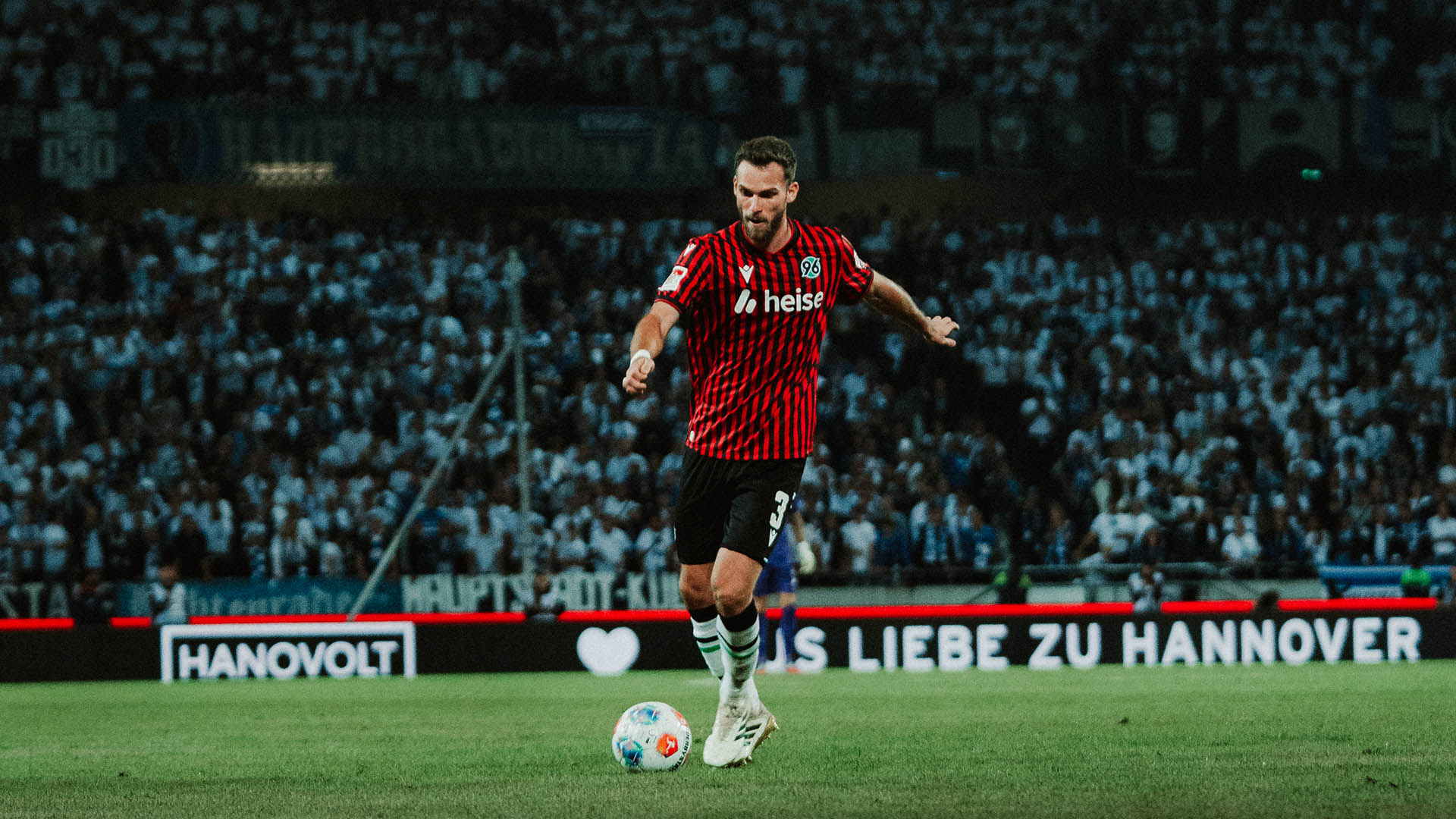Boris Tomiak läuft bei einem Abendspiel in der Heinz von Heiden Arena über den Platz. Sein rechtes Bein holt er zum Passen aus. Er trägt das rot-schwarz gestreifte Heimtrikot.