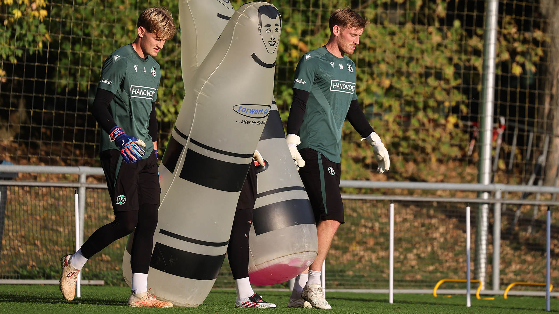Die beiden 96-Torhüter Pascal Loretz und Leo Weinkauf tragen Torhüter-Dummys auf den Trainingsplatz. 