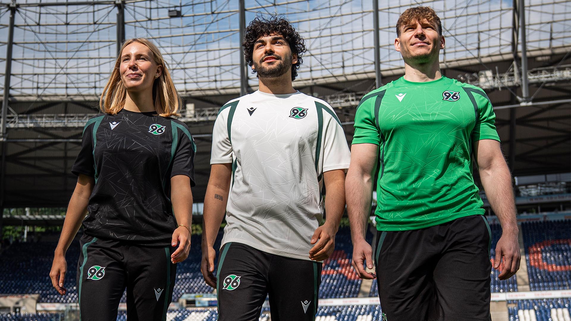 Eine Frau und zwei Männer in schwarzer, weißer und grüner Trainingskleidung im Stadion.