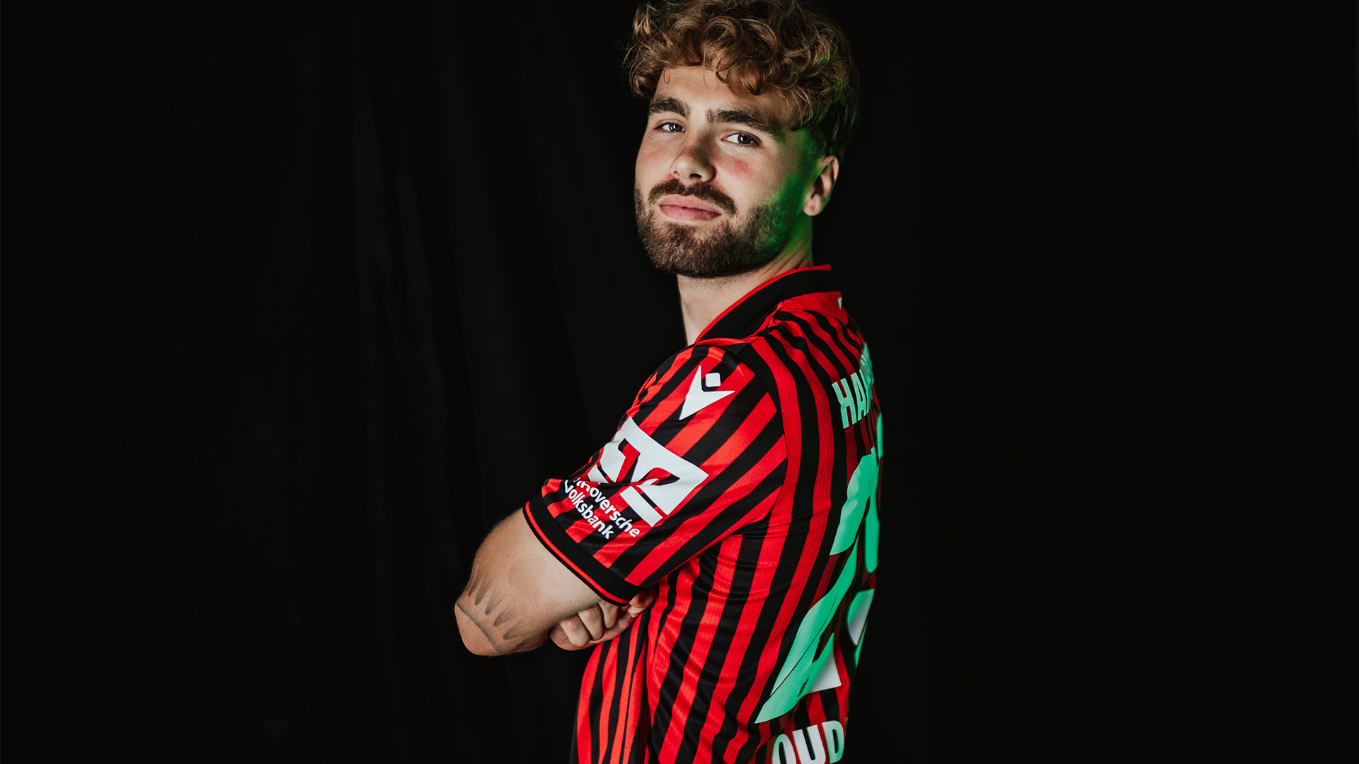 Kolja Oudenne seitlich mit verschränkten Armen vor schwarzem Hintergrund.