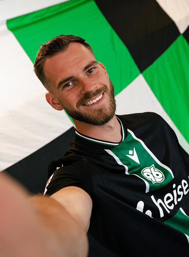 Hannover-96-Innenverteidiger Boris Tomiak trägt das neue 96-Auswärtstrikot und strahlt in die Kamera.