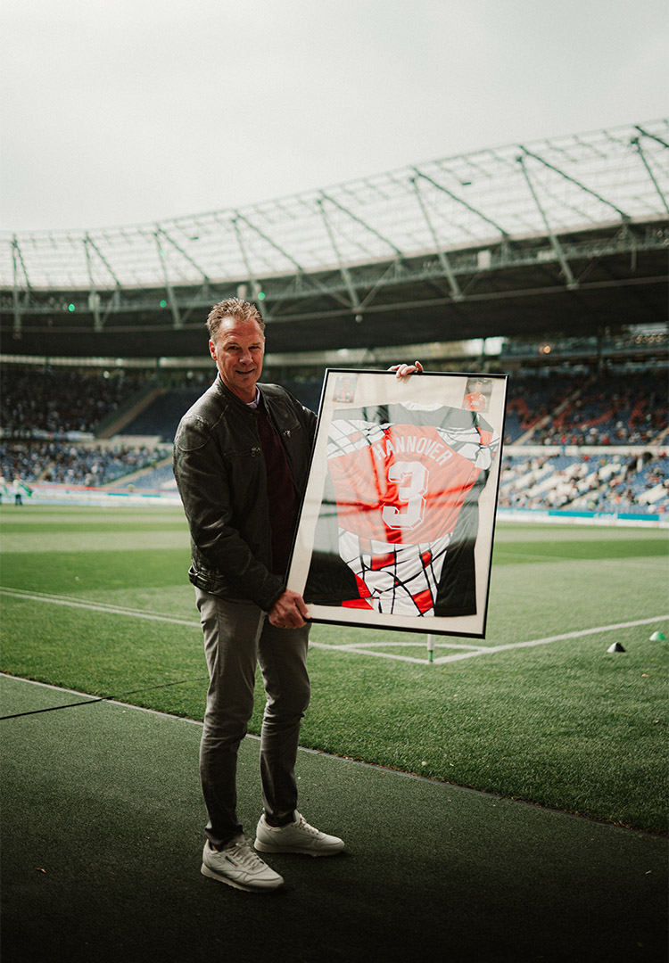 Jörg-Uwe Klütz steht am Spielfeldrand des Stadions und hält das Pokalsiegertrikot im Rahmen. 