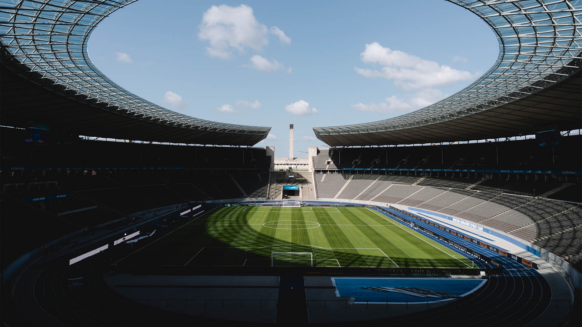 Blick ins leeren Olympiastadion bei blauem Himmel und Sonnenschein.