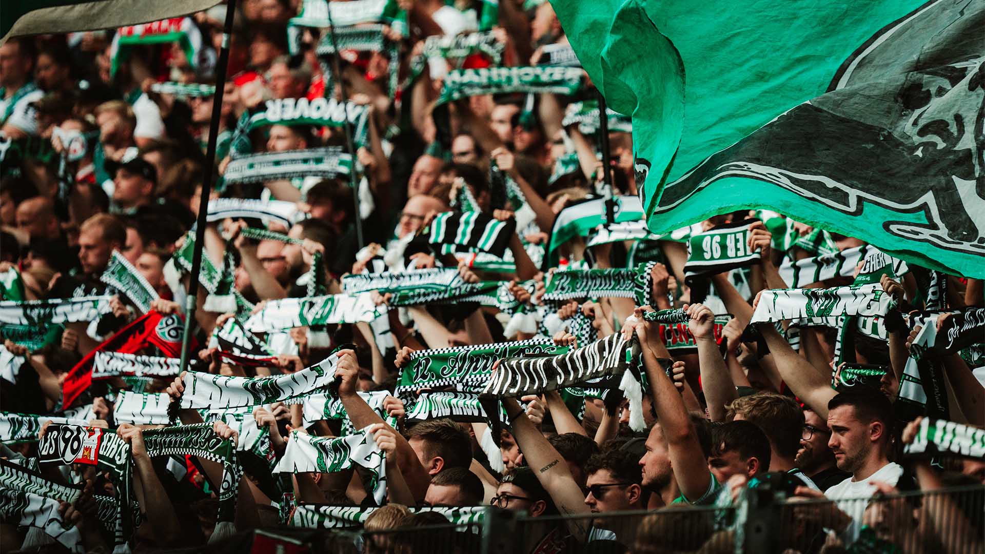 96-Fans halten Schals hoch und schwenken Fahnen.