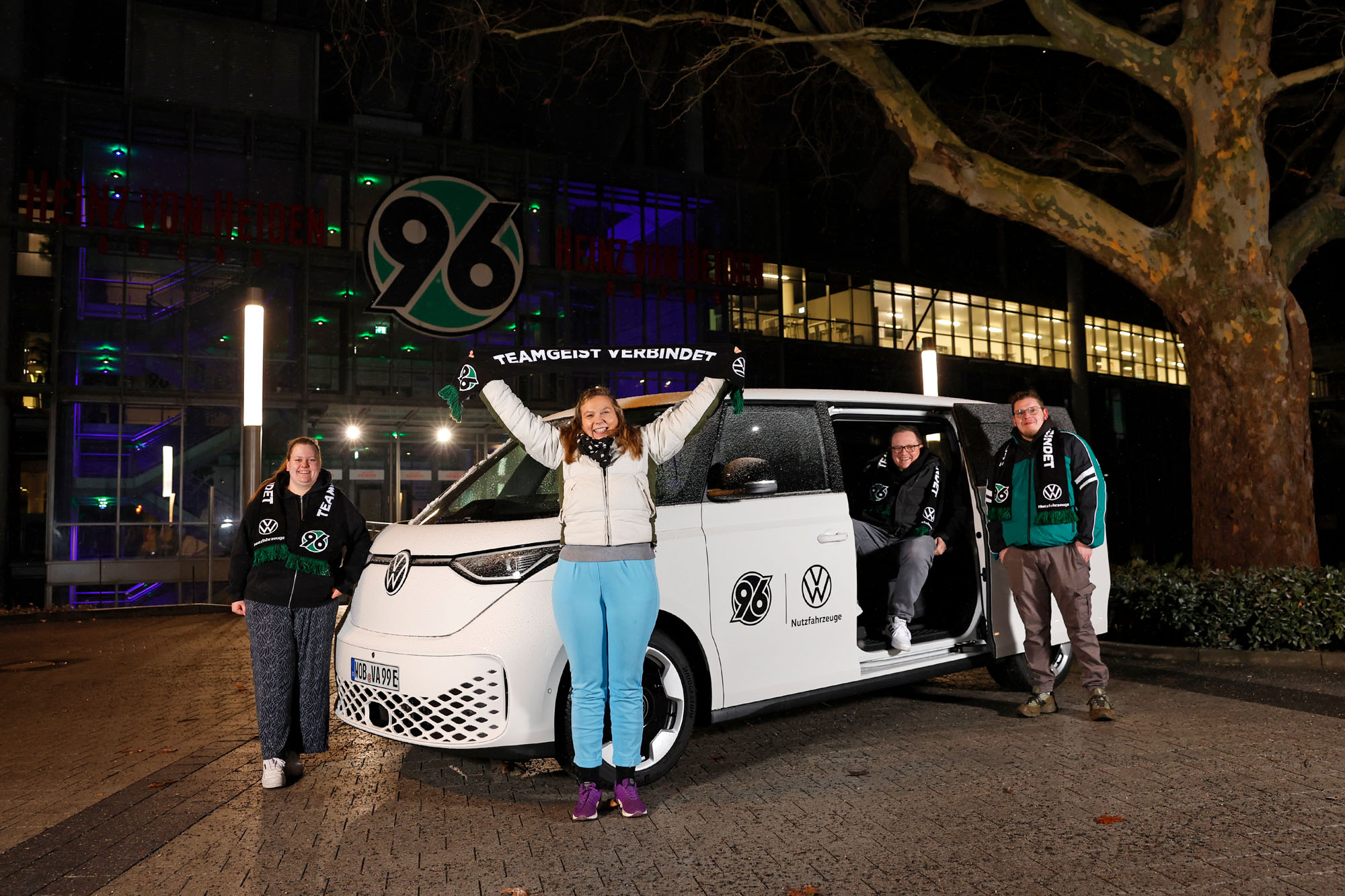 Die vier Fans stehen vor dem weißen ID. Buzz vor der Heinz von Heiden Arena, es ist dunkel.