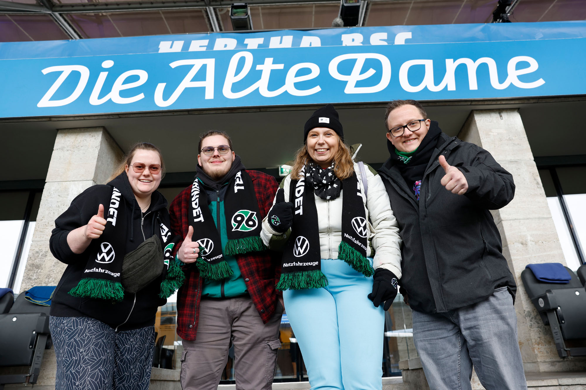 Die vier Fans stehen vor einem Schild im Olympiastadion mit der Aufschrift "Hertha BSC - Die Alte Dame".