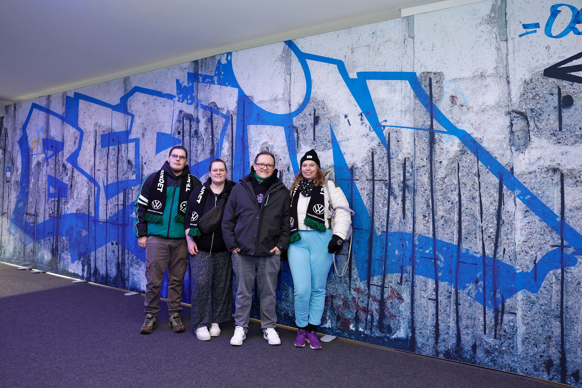 Die vier Fans stehen vor einem Graffiti im Olympiastadion.