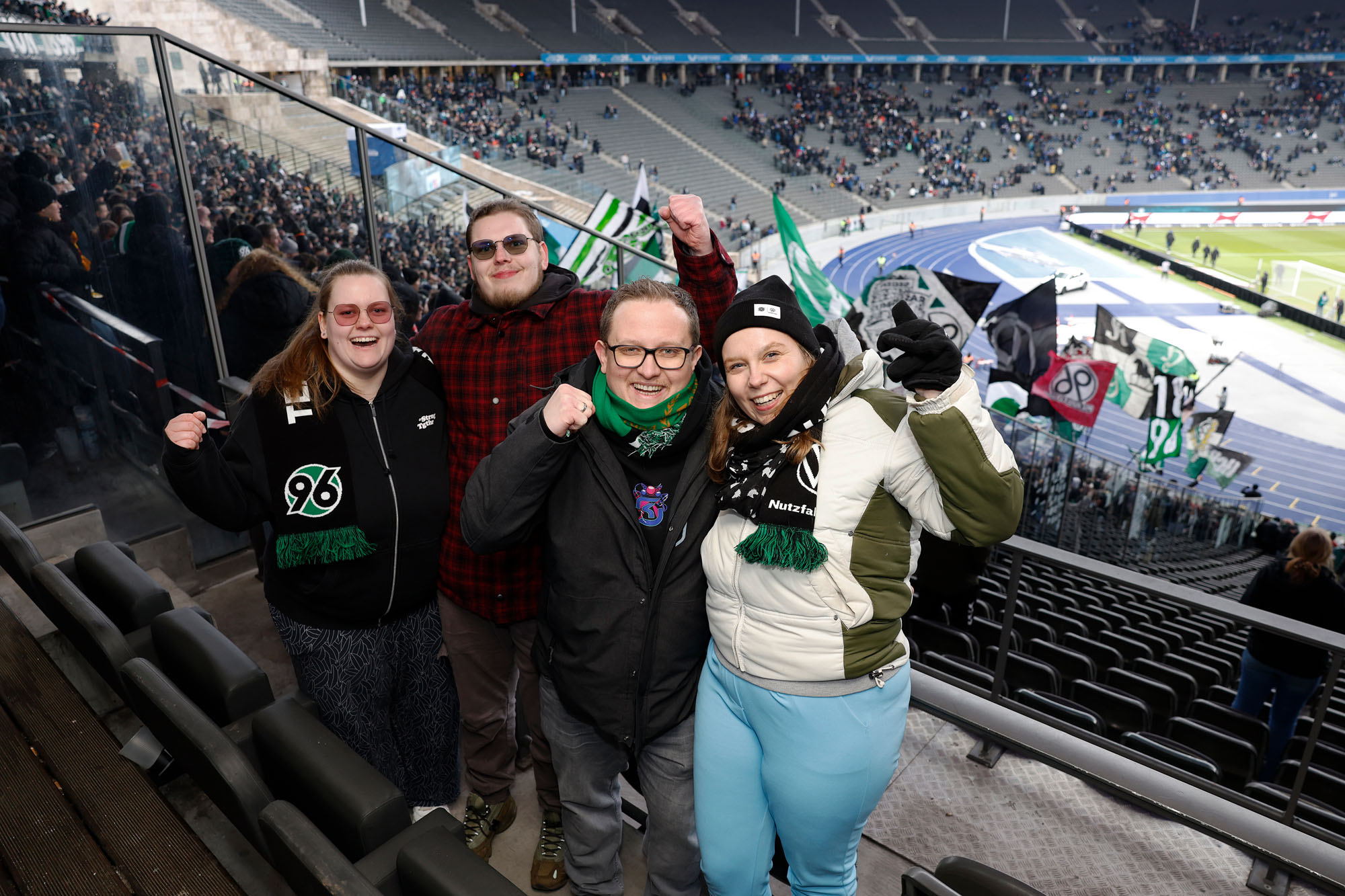 Die vier Fans stehen auf der Tribüne im Olympiastadion, im Hintergrund der volle Gästeblock.