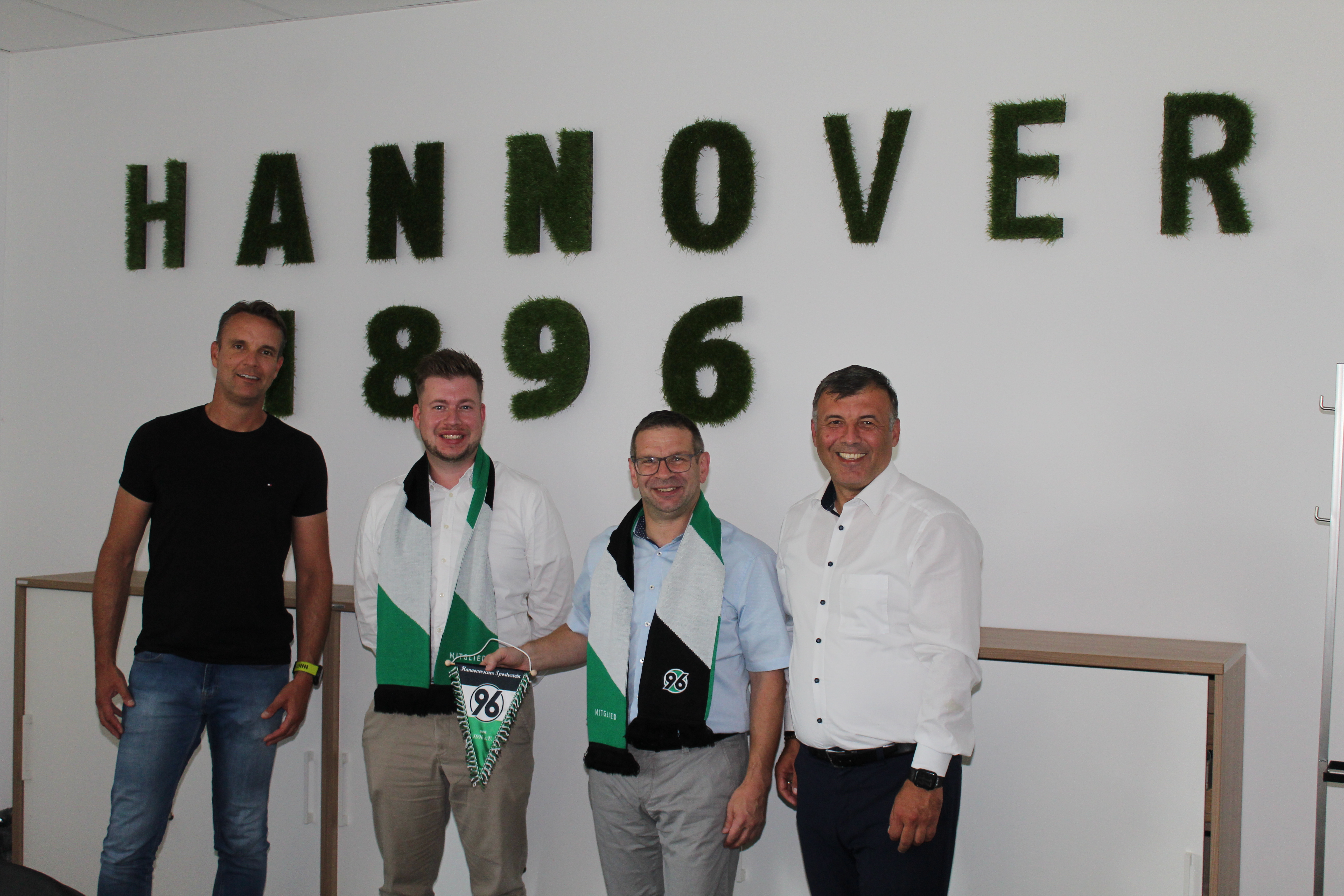 Vier Personen lächeln mit dem 96-Wimpel in der Hand in die Kamera.